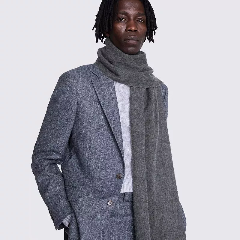 Male model wearing grey pinstripe suit with white jumper and charcoal wool scarf on studio background