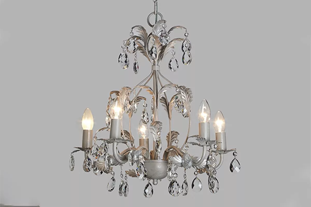 Vintage crystal chandelier with five candle bulbs, silver leaves and hanging droplets on a grey background