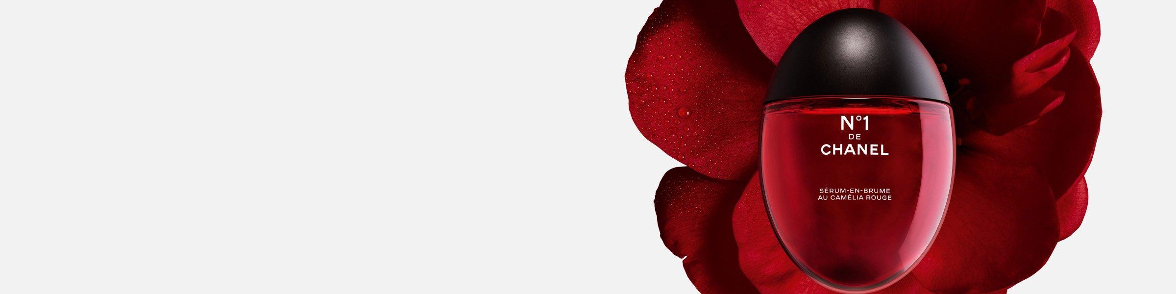 Chanel No. 1 red serum mist bottle placed in front of a dewy red camellia flower.