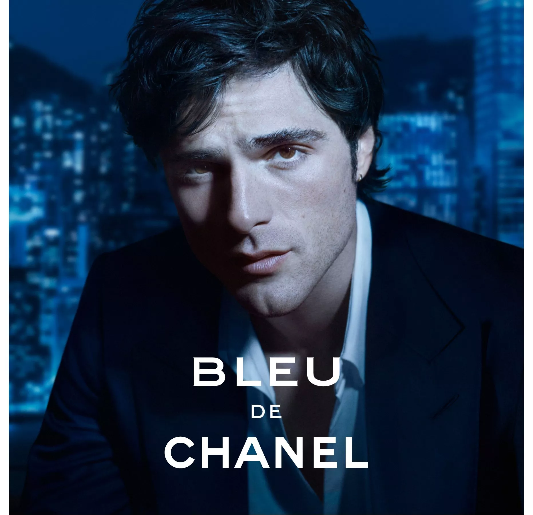Bleu de Chanel fragrance advert featuring a man in a dark suit against a blue city skyline background.