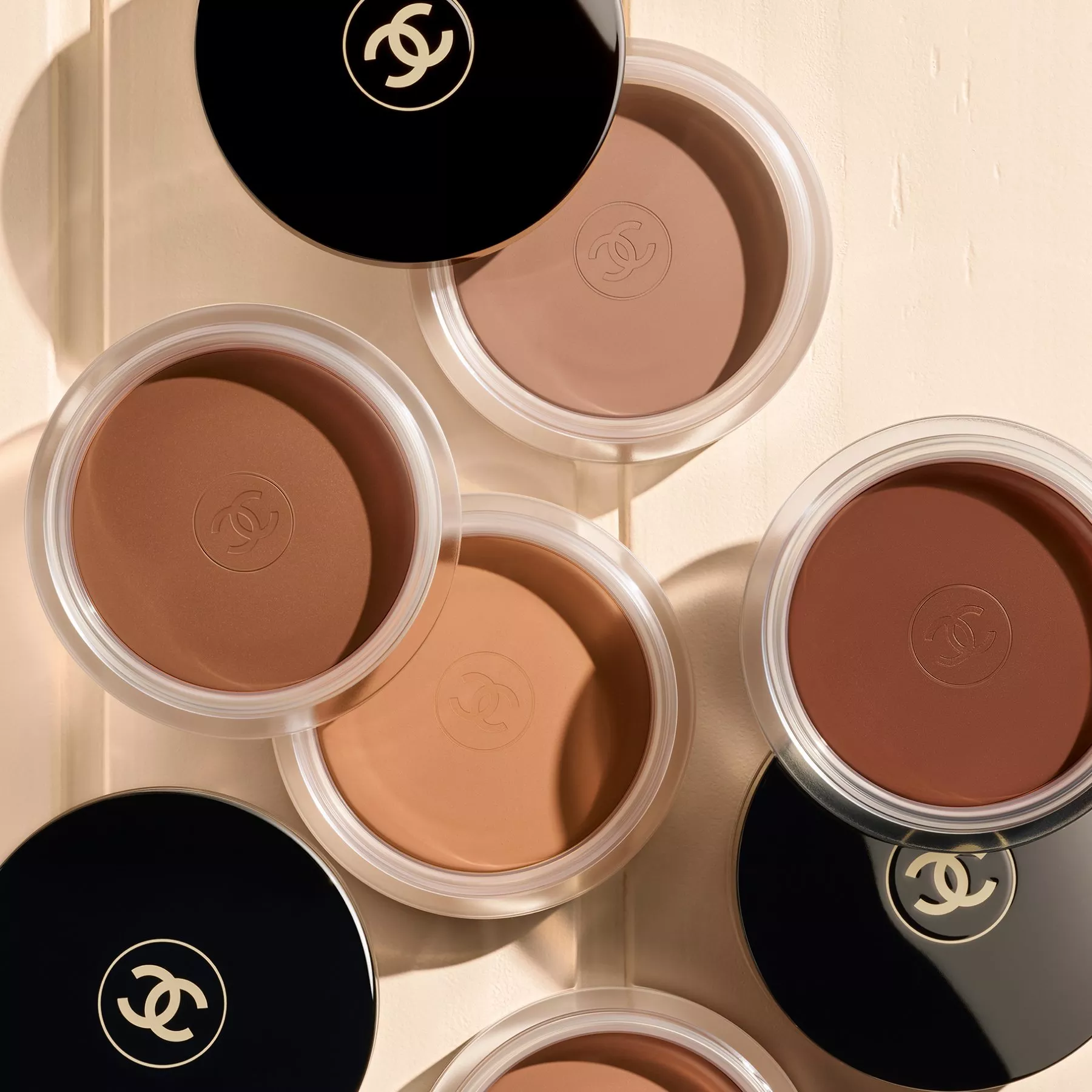 Top view of luxury bronzing powder compacts in multiple shades, arranged on a neutral background in soft light