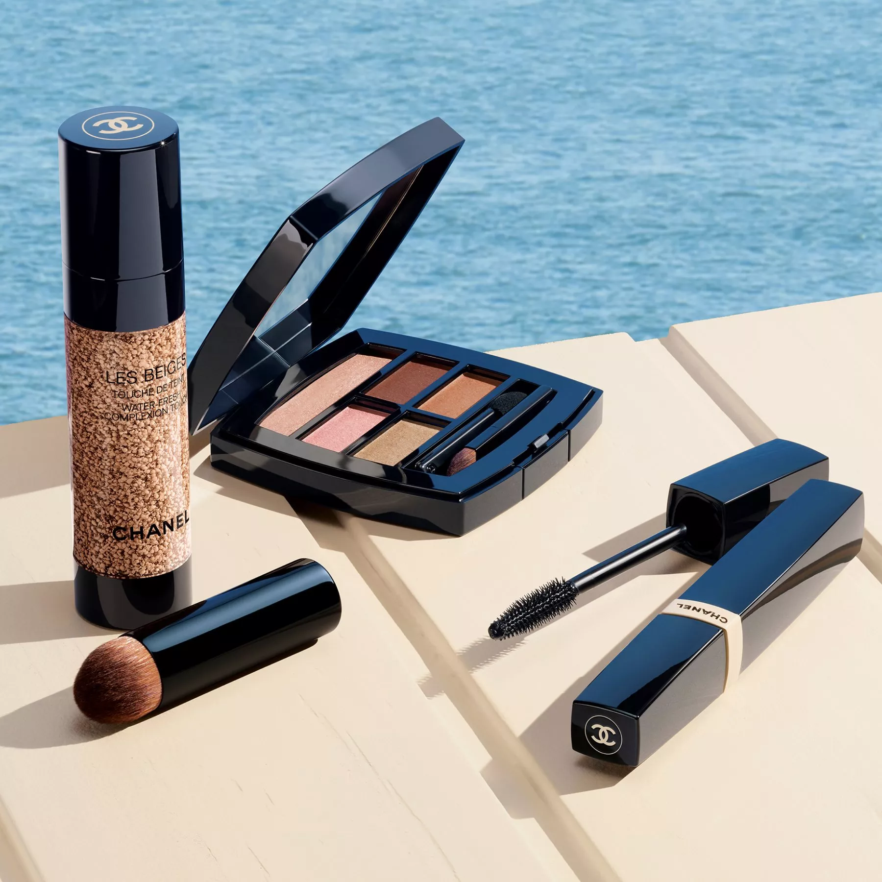 Chanel makeup set by the sea: Les Beiges foundation, eyeshadow palette, brush and mascara on a sunlit deck