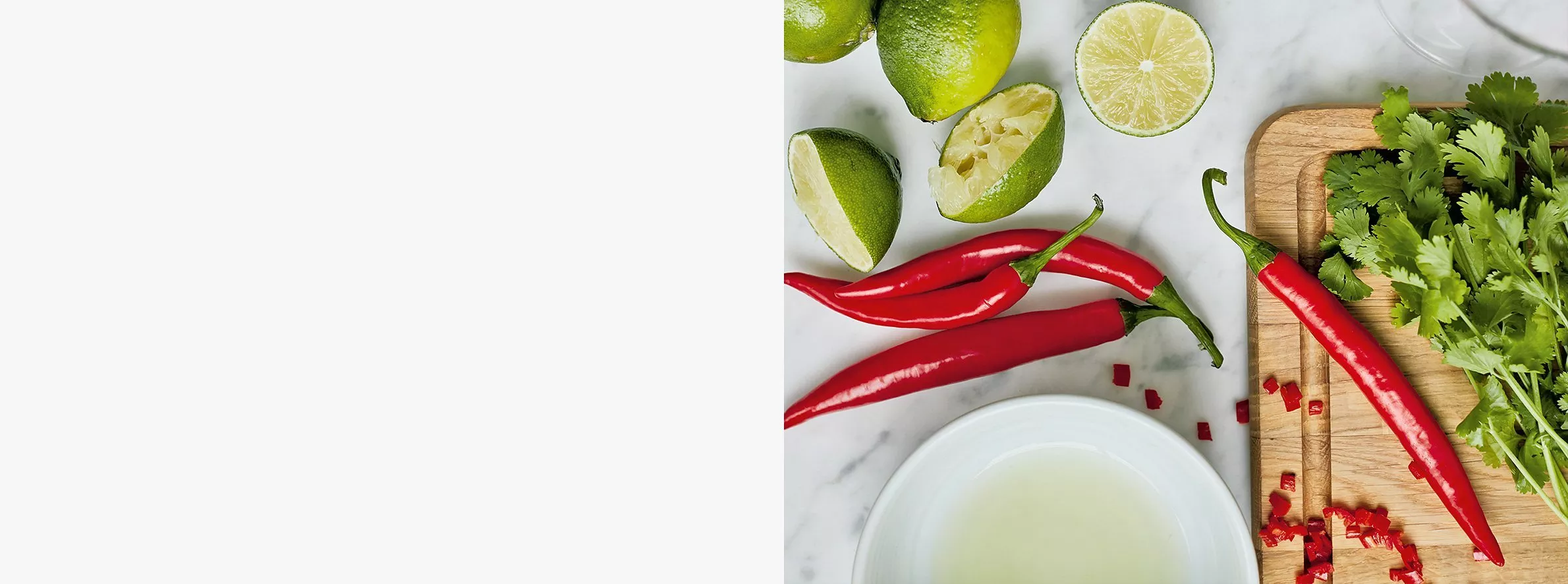 Fresh limes, red chillies and coriander on a chopping board, top-down on marble kitchen counter background