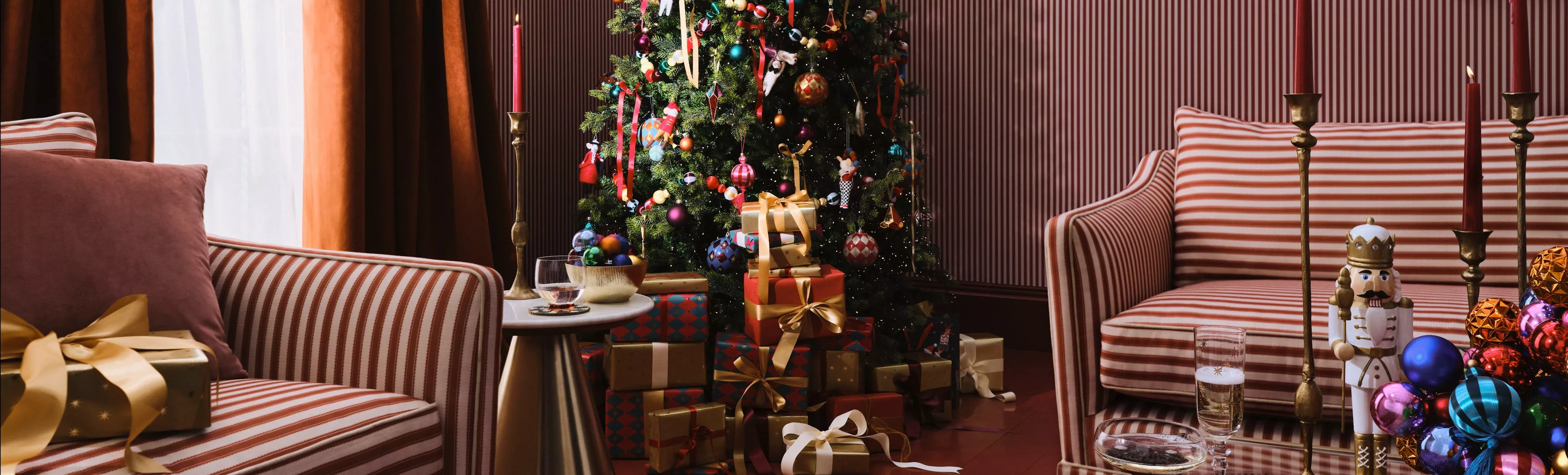 Cosy Christmas living room with decorated tree, wrapped presents, striped armchairs, candles and baubles.