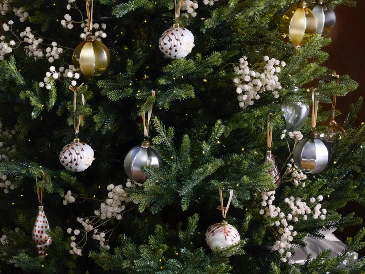 Close-up of Christmas tree with gold and silver baubles, white floral garland and warm fairy lights indoors