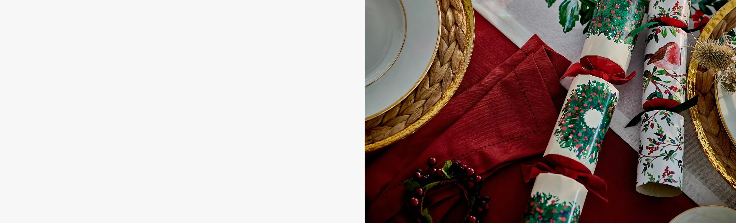 Festive Christmas table setting with red and white patterned crackers on plate, holly berries and rustic linen.