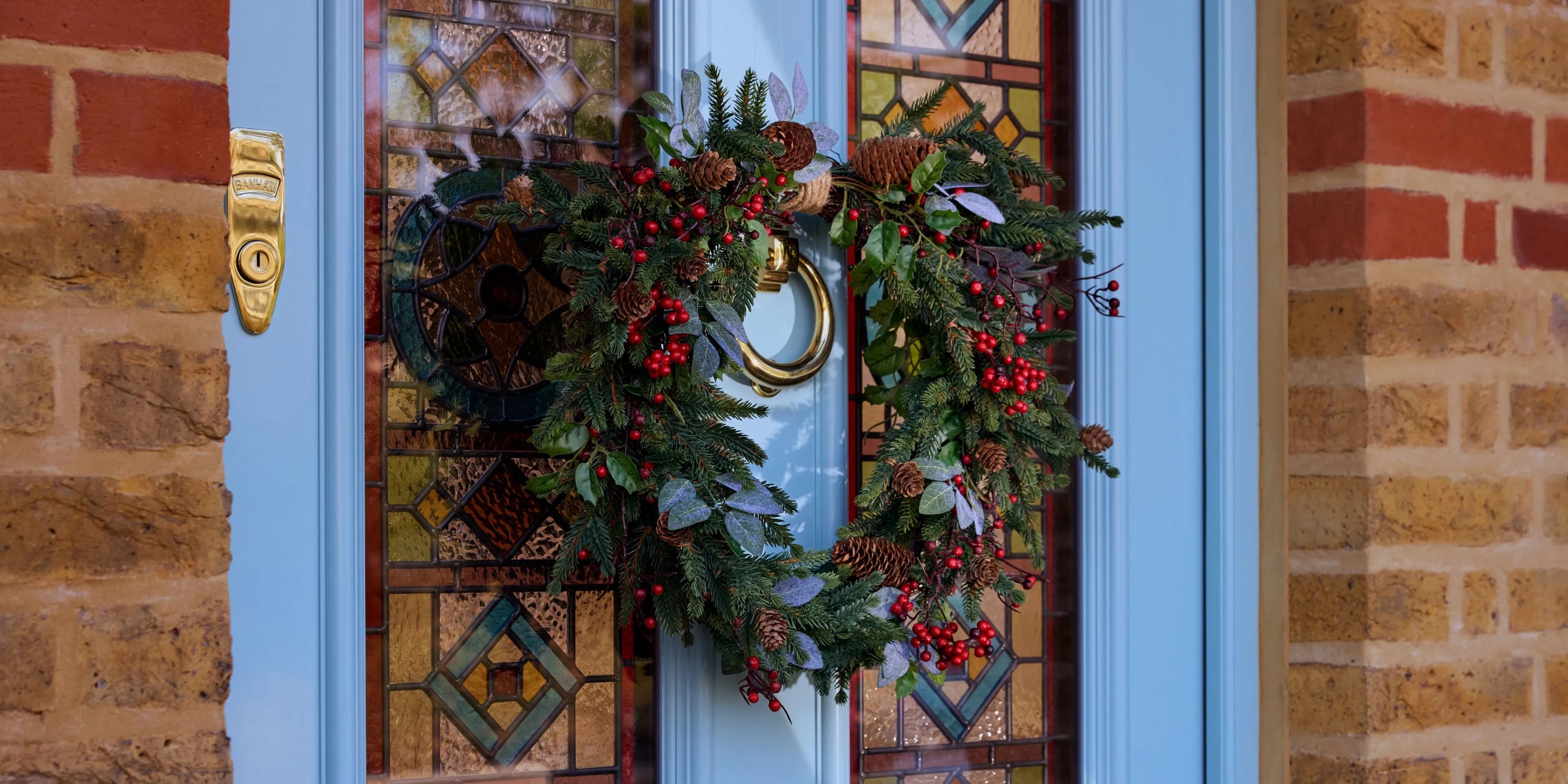 Christmas wreath with pine cones and red berries on a blue front door with stained glass panels and brass knocker