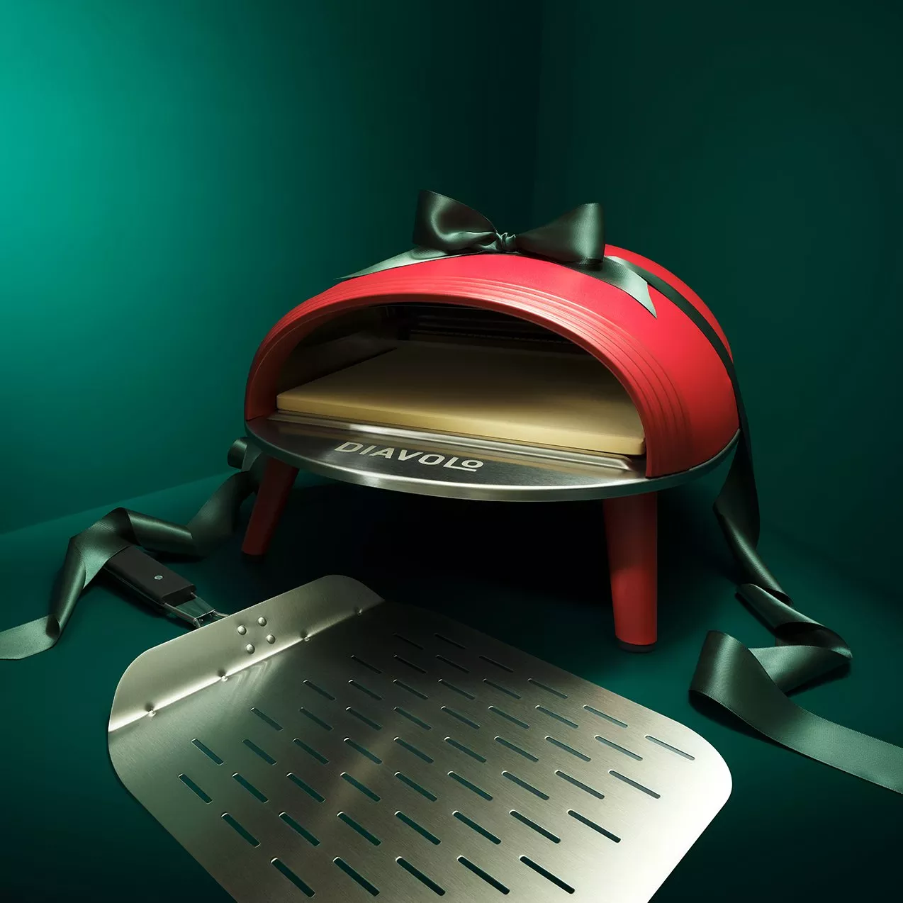 Red Diavolo tabletop pizza oven with black bow ribbon and metal pizza peel on teal background, gift idea