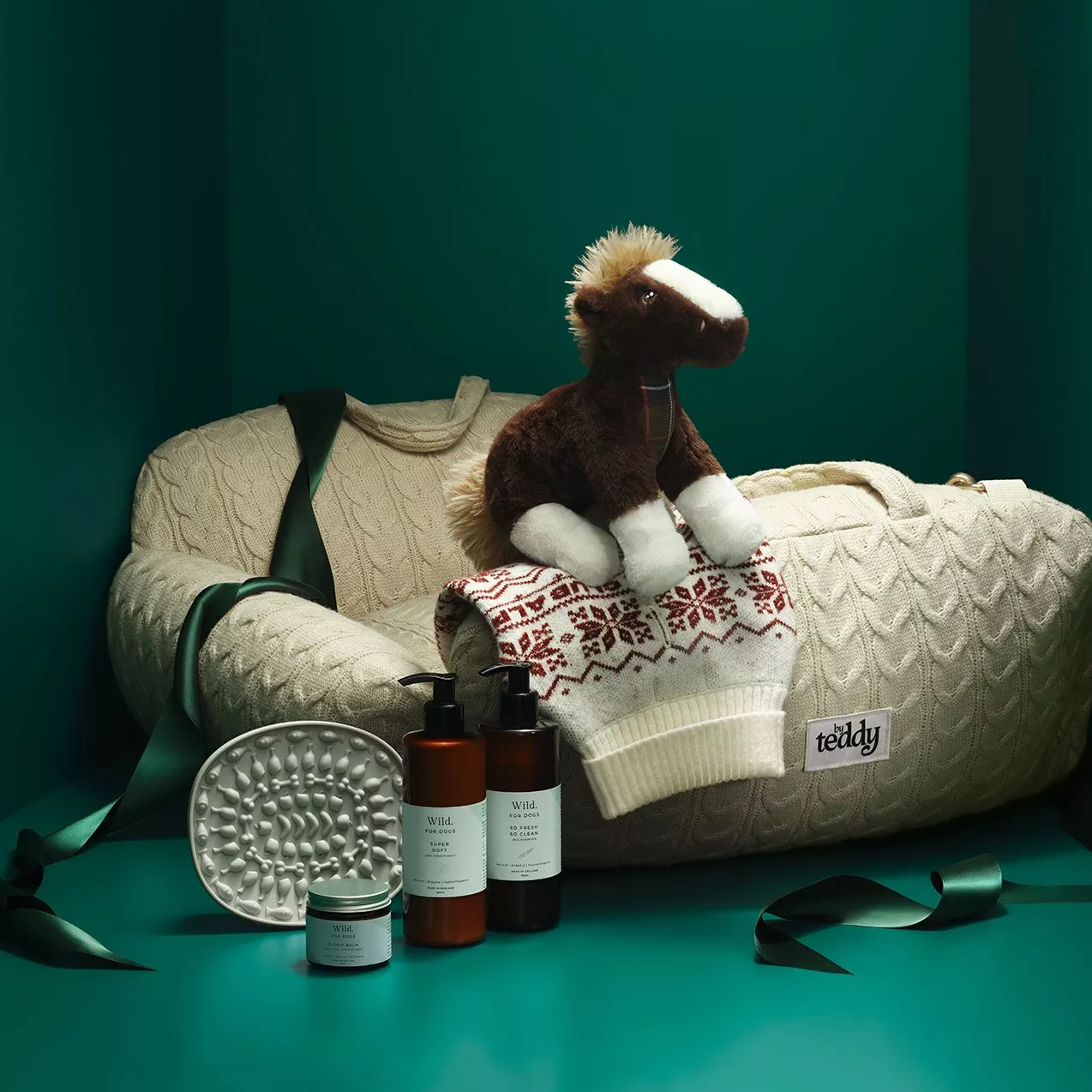Dog grooming gift set with shampoo, conditioner and balm beside cosy knit dog bed and plush horse toy