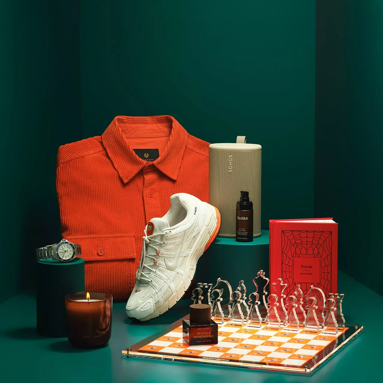 Stylish gift flat lay with orange corduroy shirt, white trainers, chess set, candle, speaker, watch and book