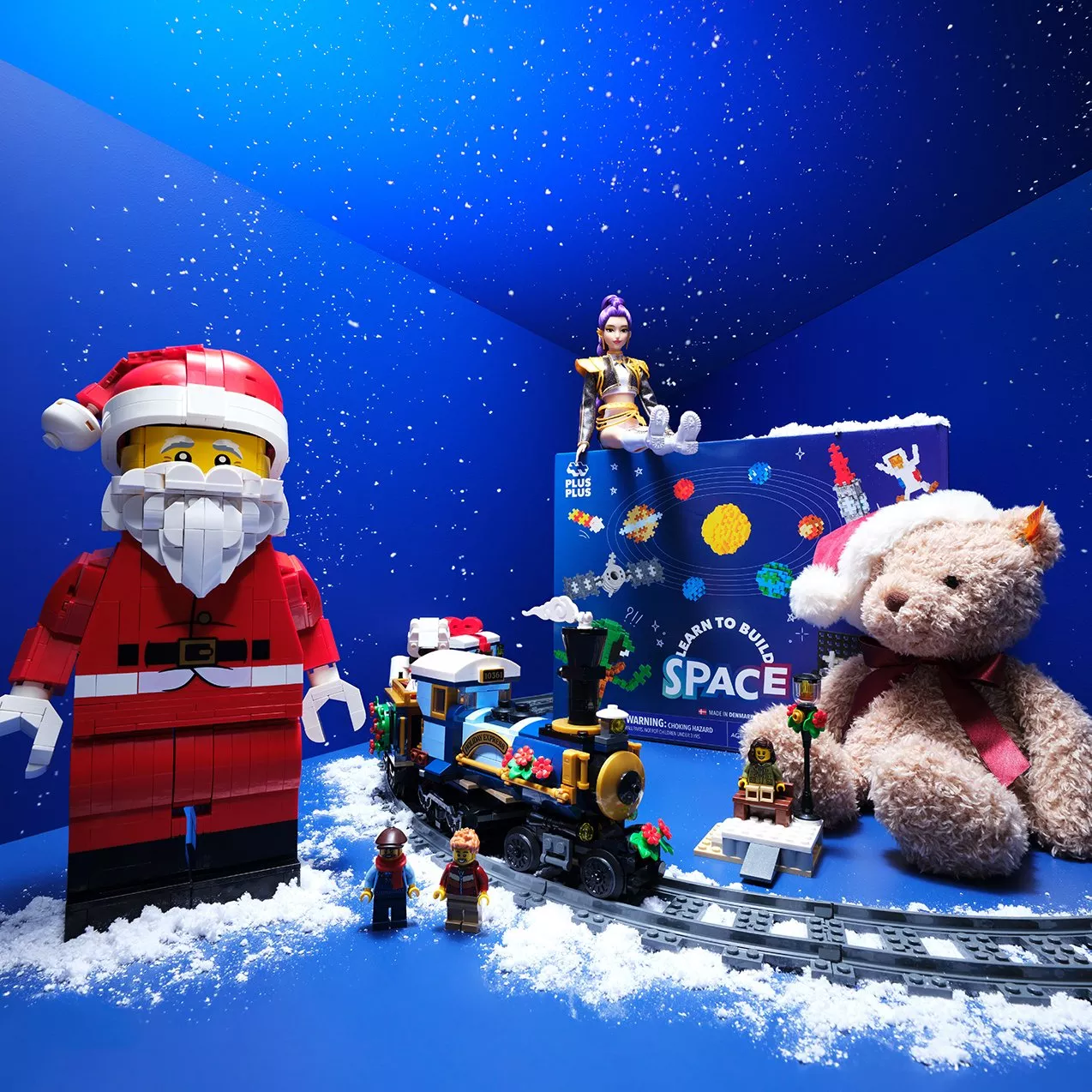 Festive LEGO Santa and Christmas toy train display with teddy bear, snowy backdrop and space-themed box