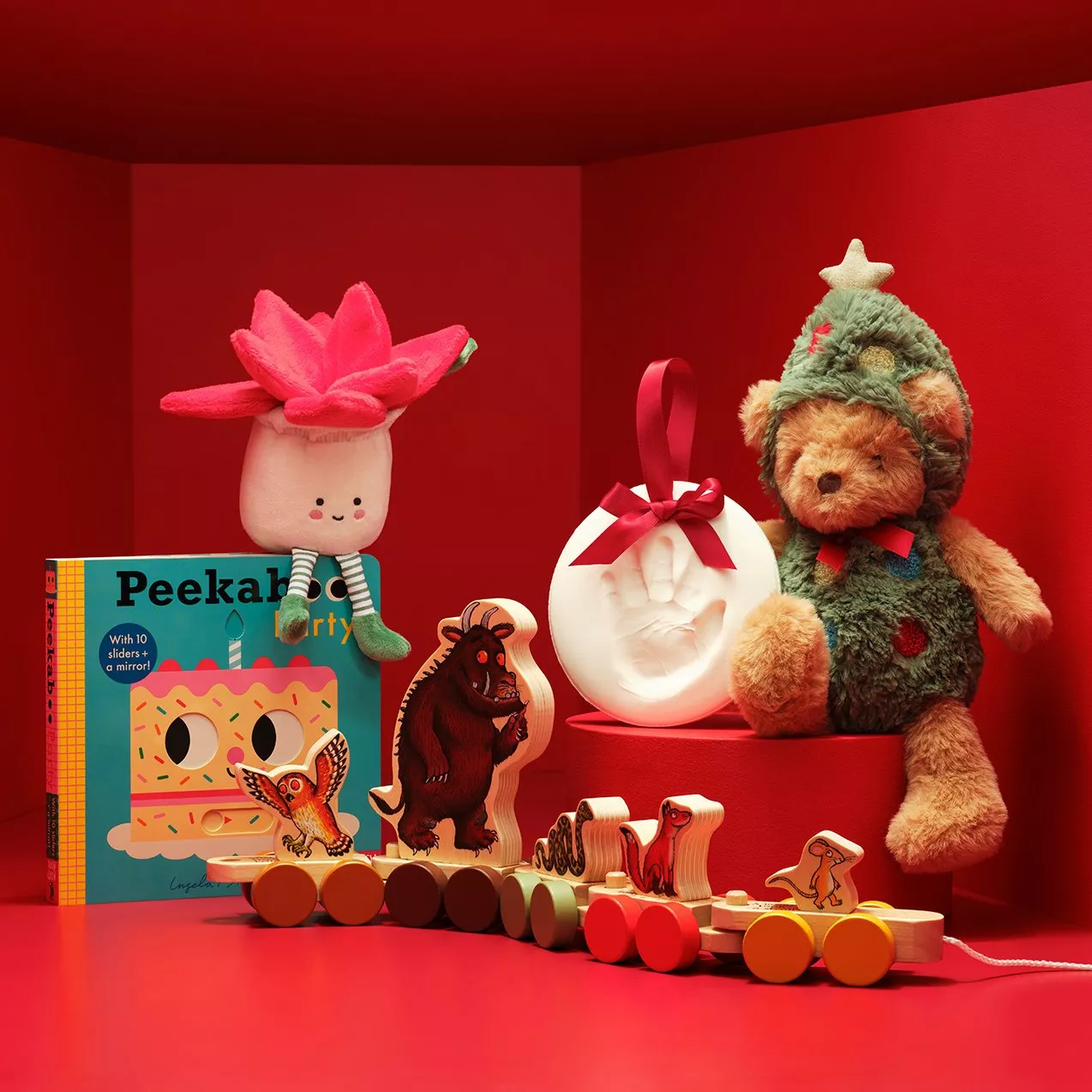 Christmas gift hamper with teddy bear, baby handprint keepsake, wooden animal train and Peeka book on red backdrop