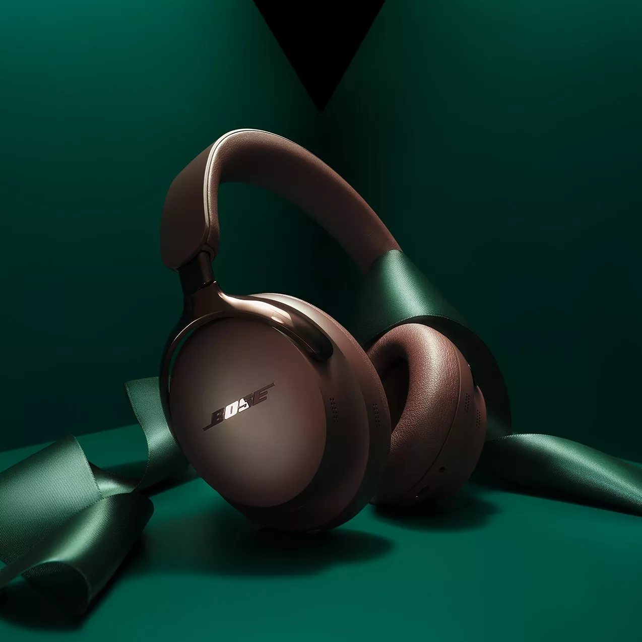 Bose over-ear wireless noise-cancelling headphones in bronze on green background with festive ribbon wrap