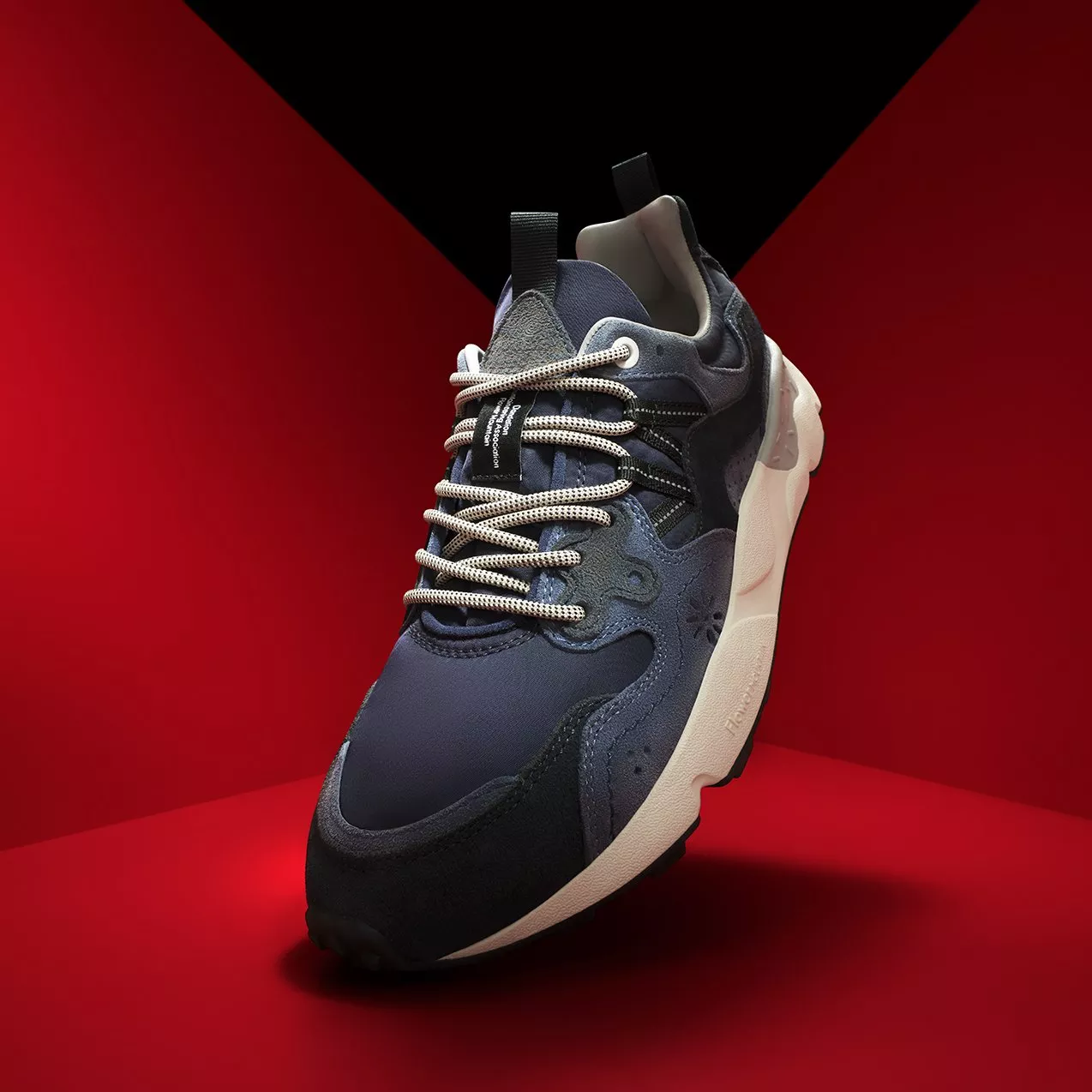 Navy and black running trainer with white laces and chunky sole, studio product photo on red background