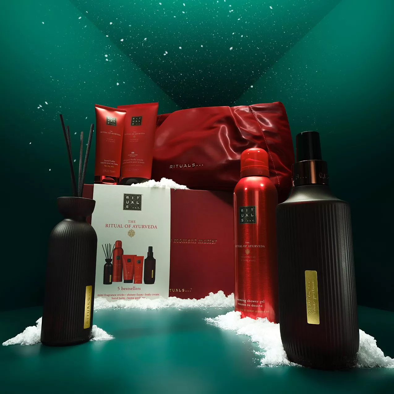 Rituals Ayurveda gift set with red toiletries, diffuser bottles and pouch, styled with snow on green backdrop