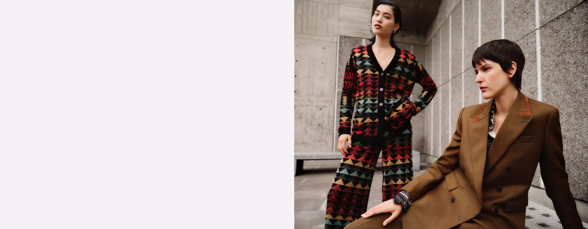 Two individuals in stylish outfits: one in a bold, geometric patterned ensemble, the other in a tailored brown suit.