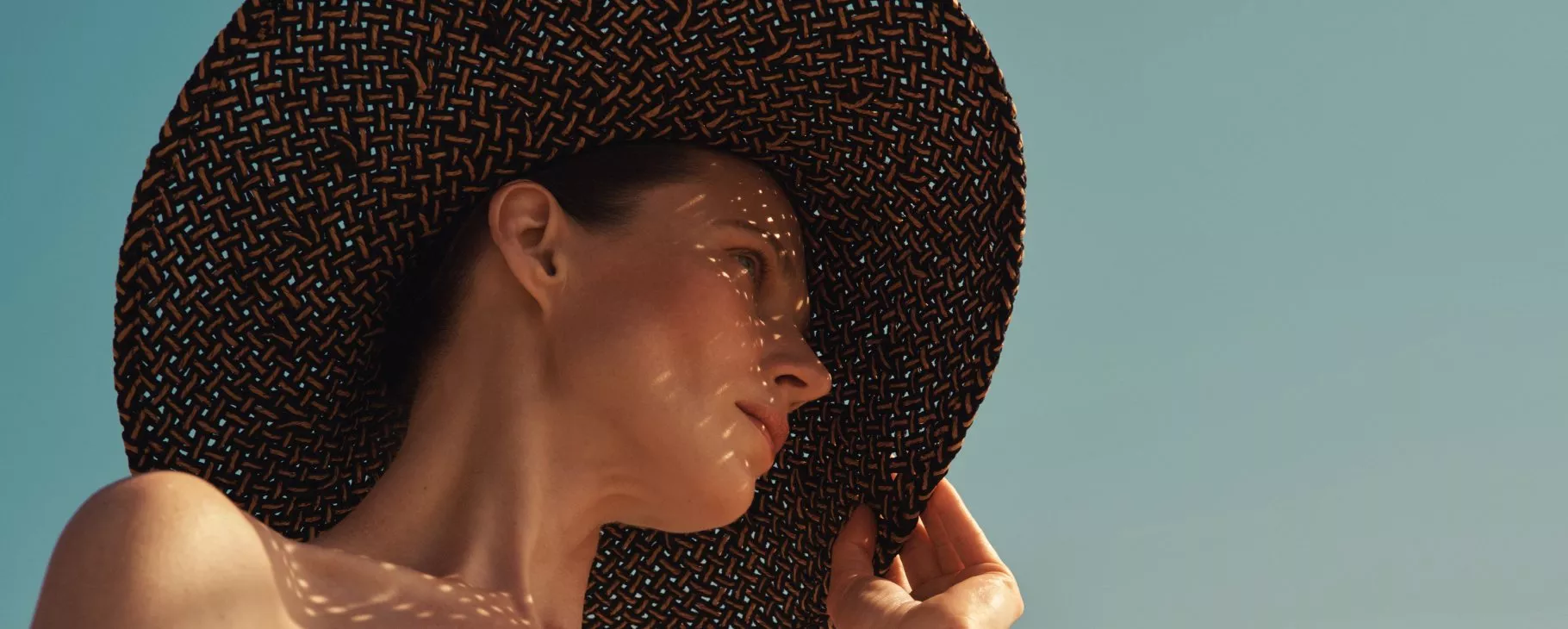 Portrait of a woman in a wide-brim straw sunhat with dappled light, clear blue sky, summer holiday mood