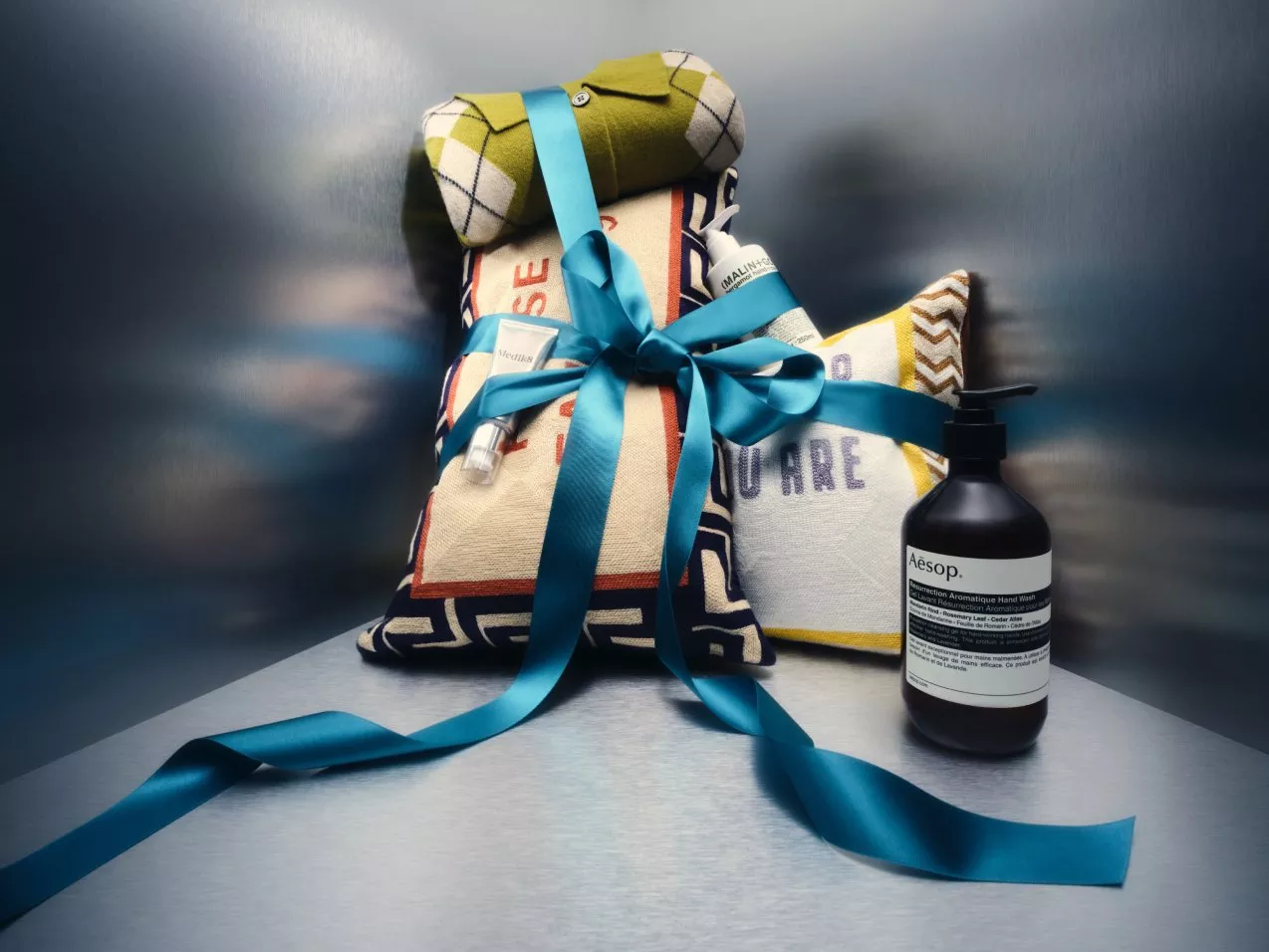 Pillows wrapped with a ribbon in a mirrored corner with an Aesop hand wash beside them