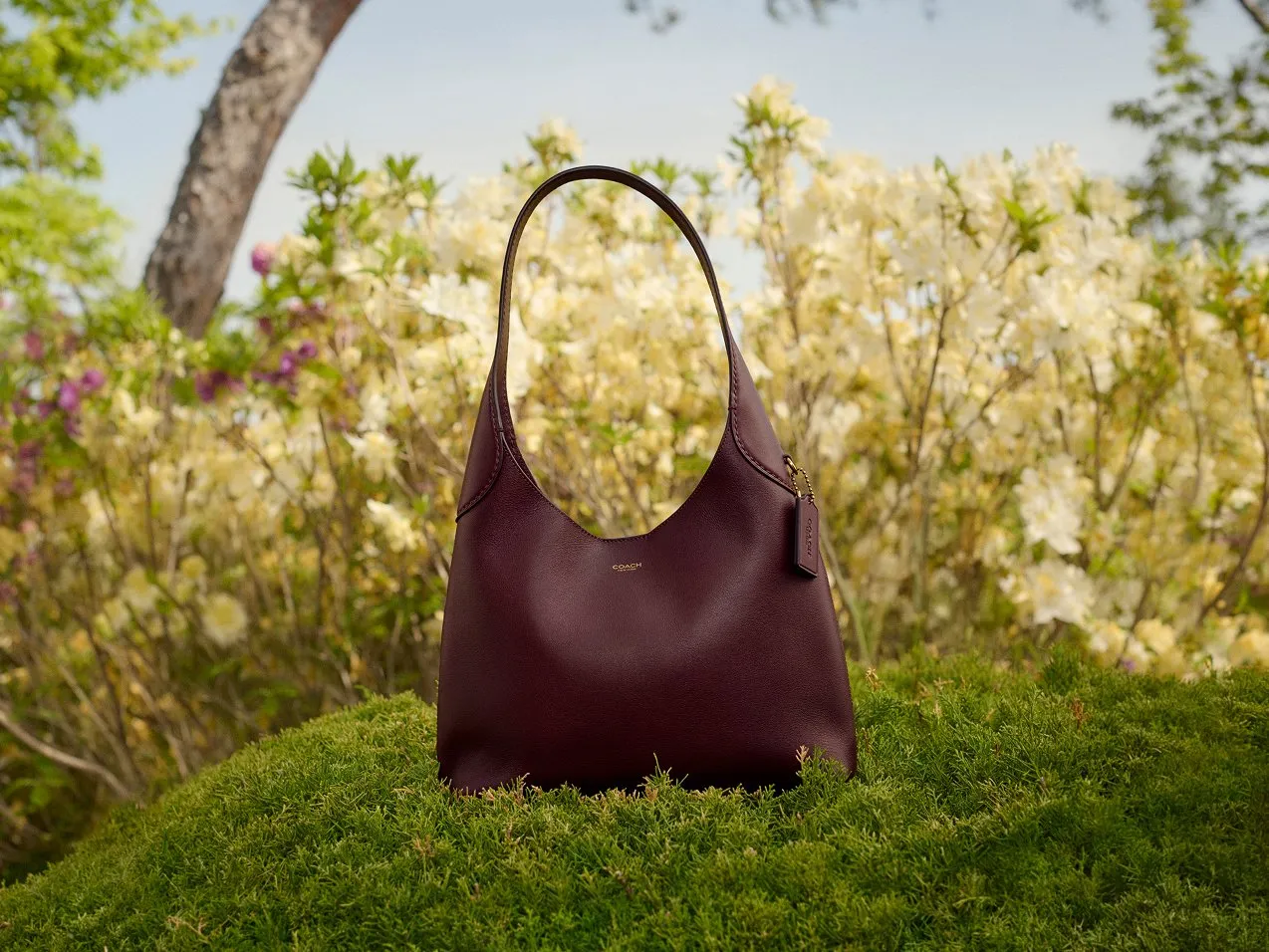 Burgundy leather hobo handbag on moss with spring blossom background
