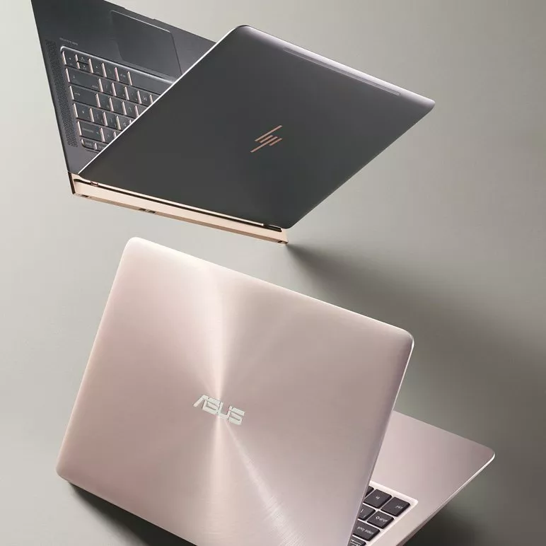 Two premium laptops, ASUS and HP, shown in rose gold and dark grey with metallic finish on a desk