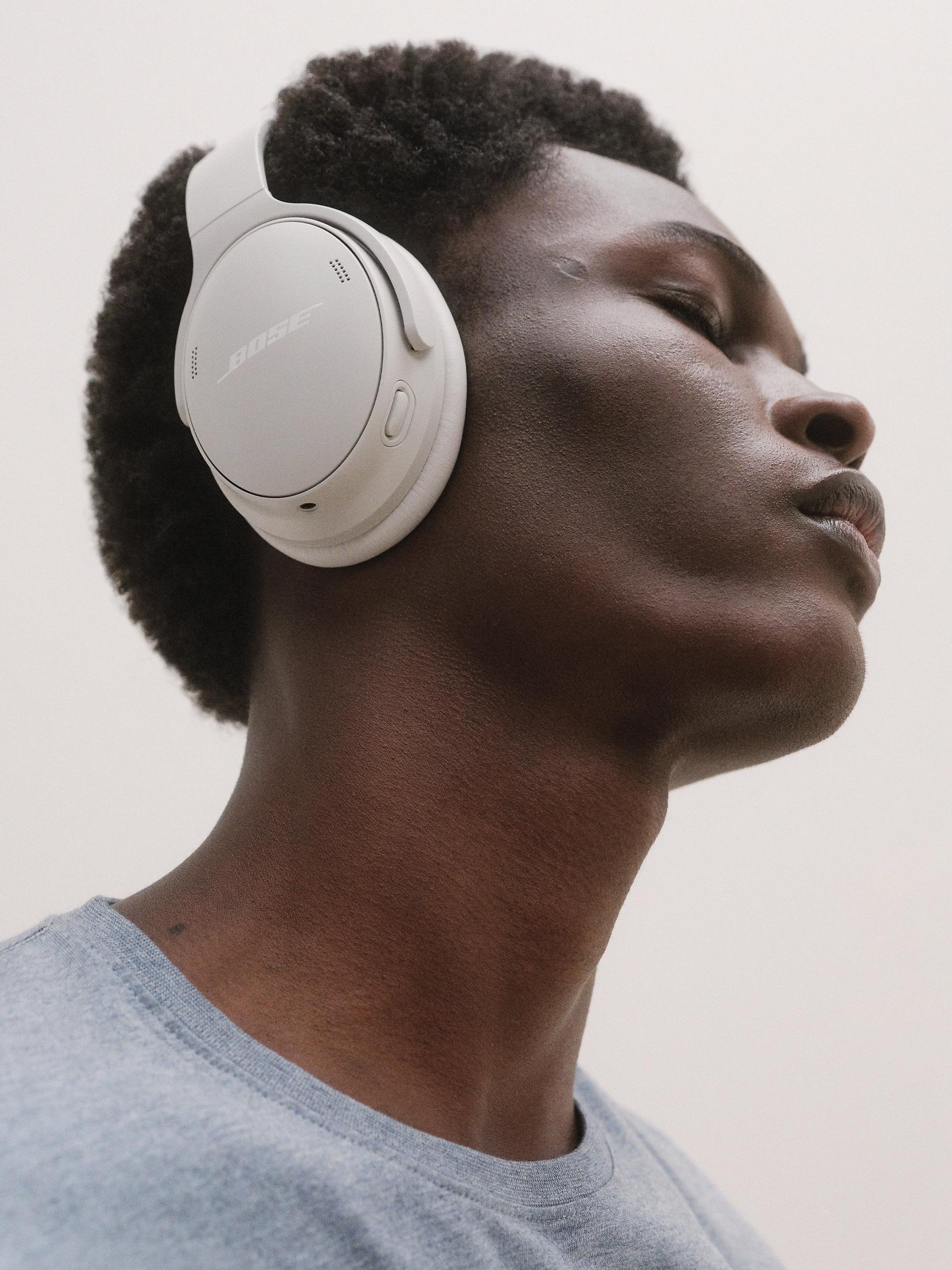 Close-up of a man wearing white Bose noise-cancelling wireless headphones, eyes closed, enjoying music outdoors