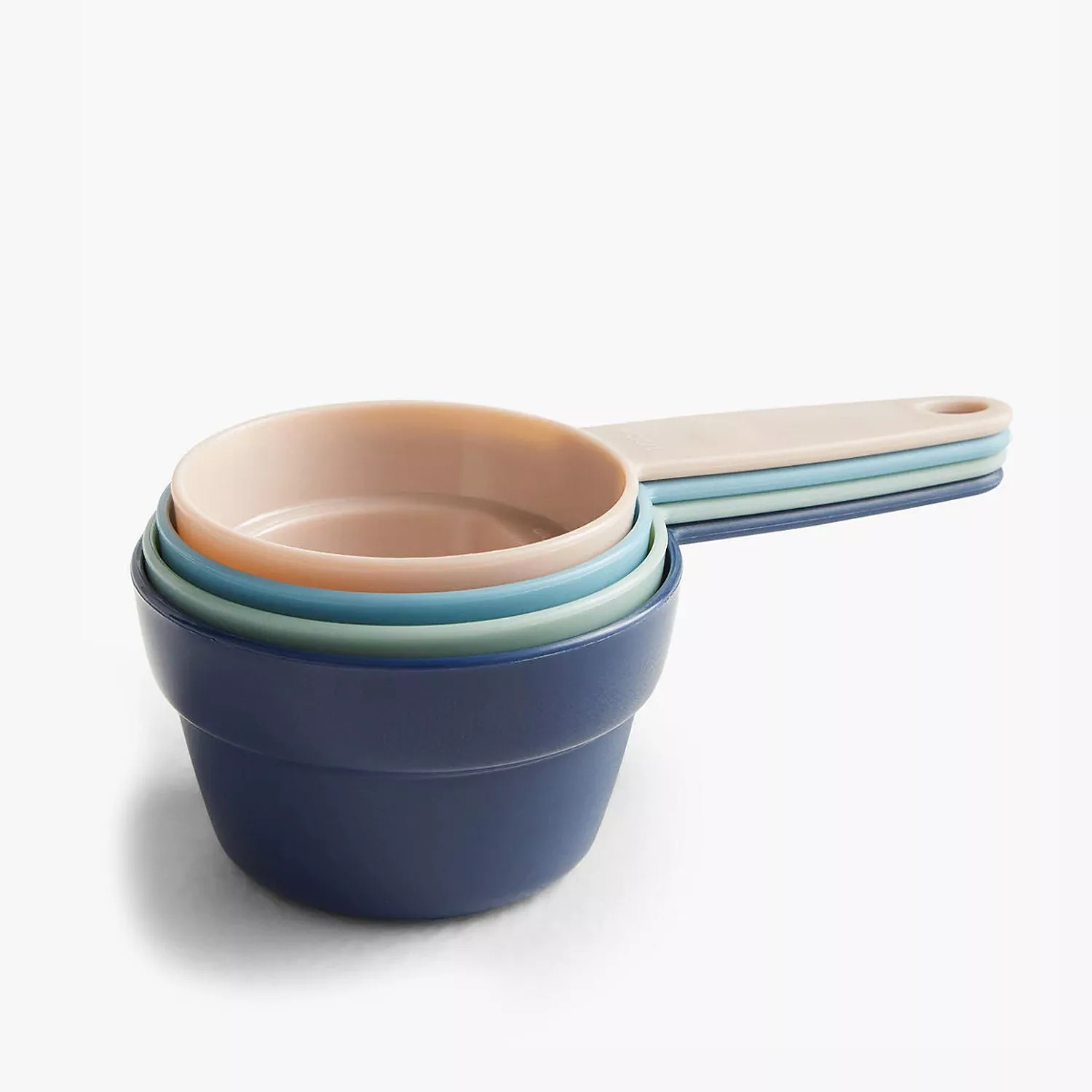 Stacked pastel measuring cups with handles, plastic kitchen baking set in blue, green and pink on white background