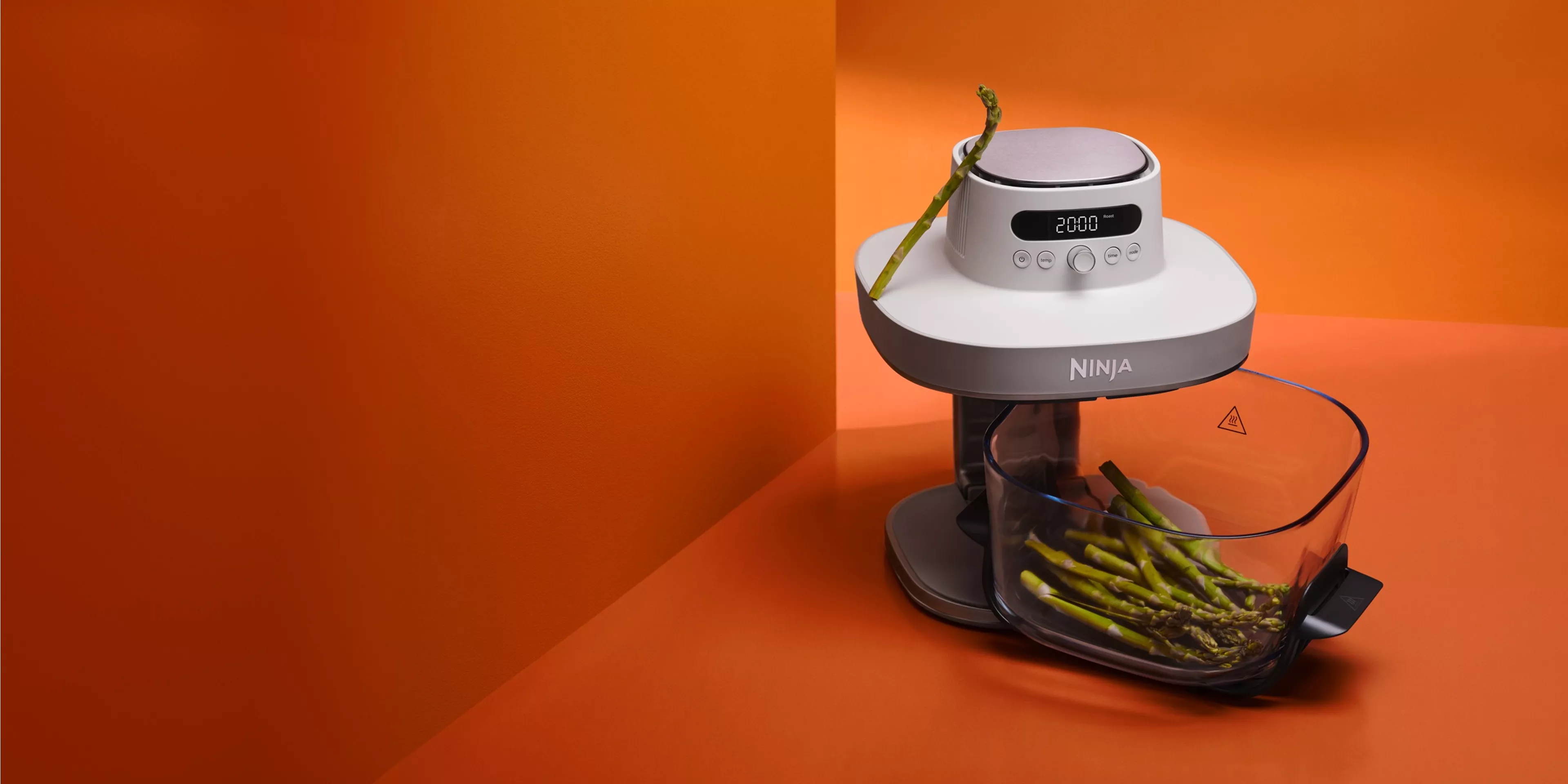 Ninja food processor with digital timer, chopping fresh asparagus spears in clear bowl on orange background