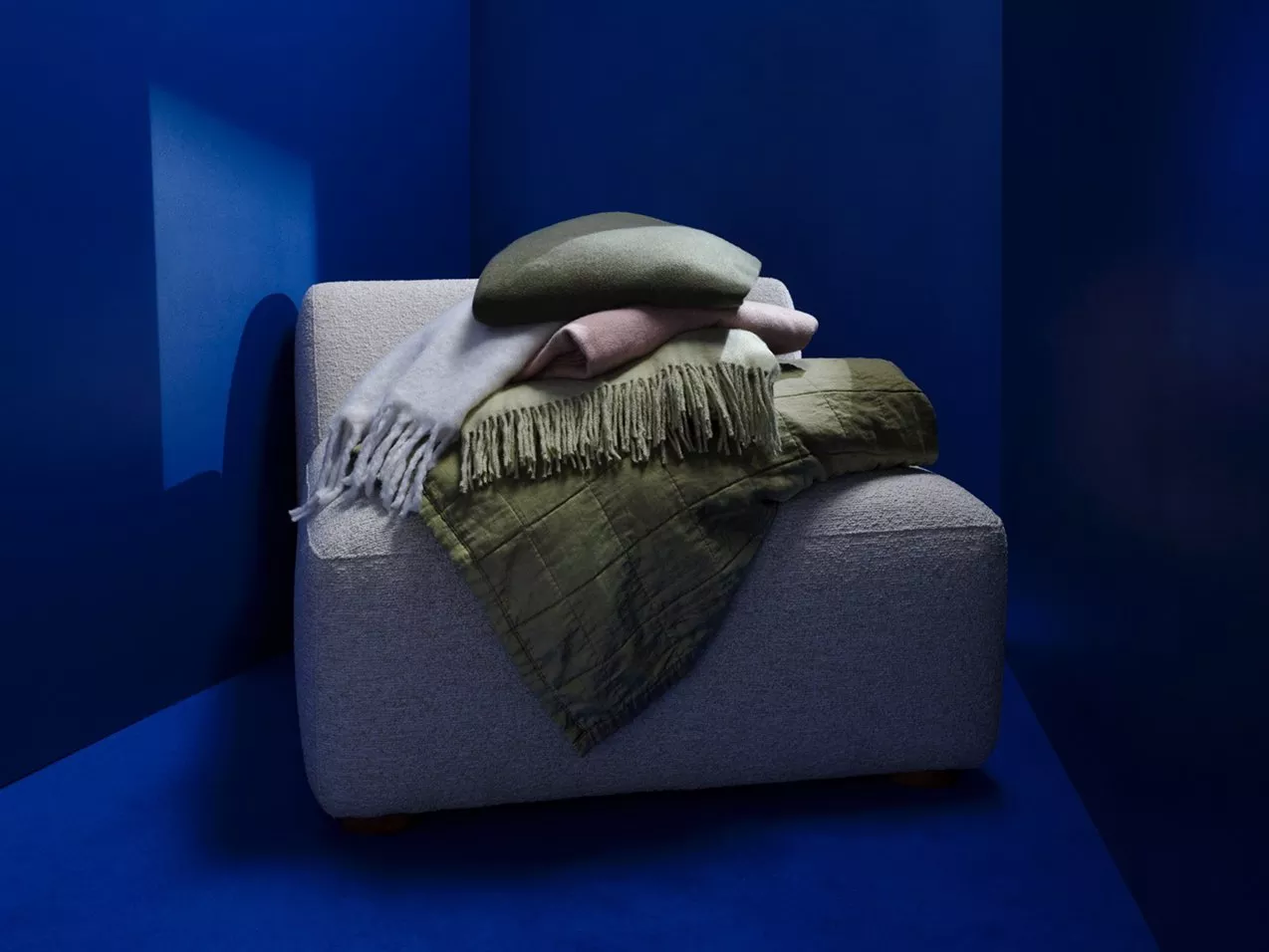 Grey upholstered armchair with folded blankets and cushions in a blue room, cosy modern home décor styling