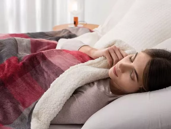 Young woman sleeping in bed under a cosy fleece blanket, restful bedroom scene for comfort and better sleep