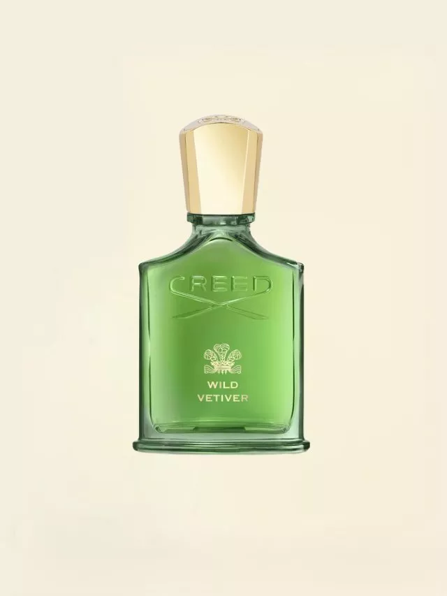 Creed Wild Vetiver bottle with a green hue, featuring a gold cap and elegant branding on a soft beige background.
