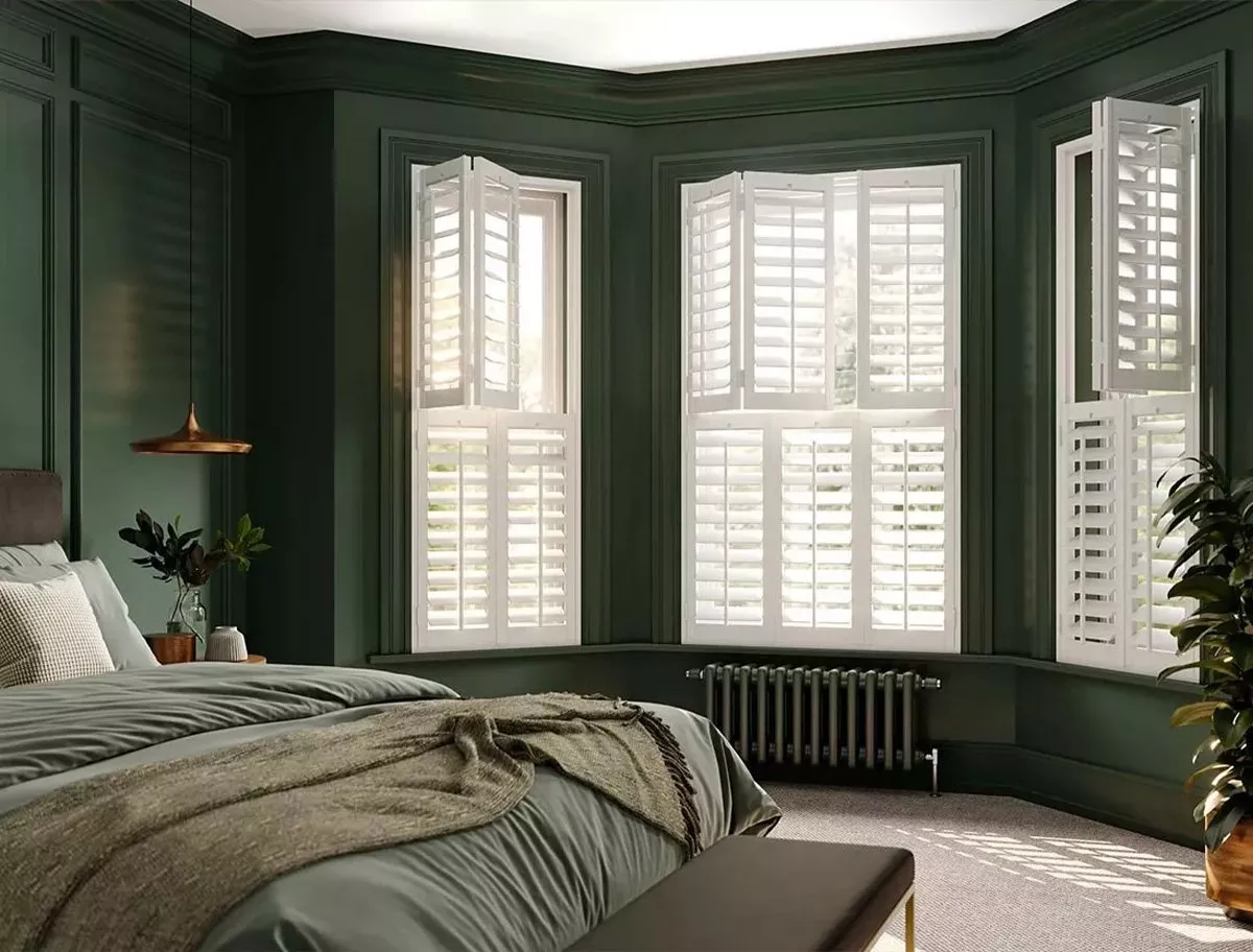 Bedroom with dark green walls and white wooden shutters on the bay window.