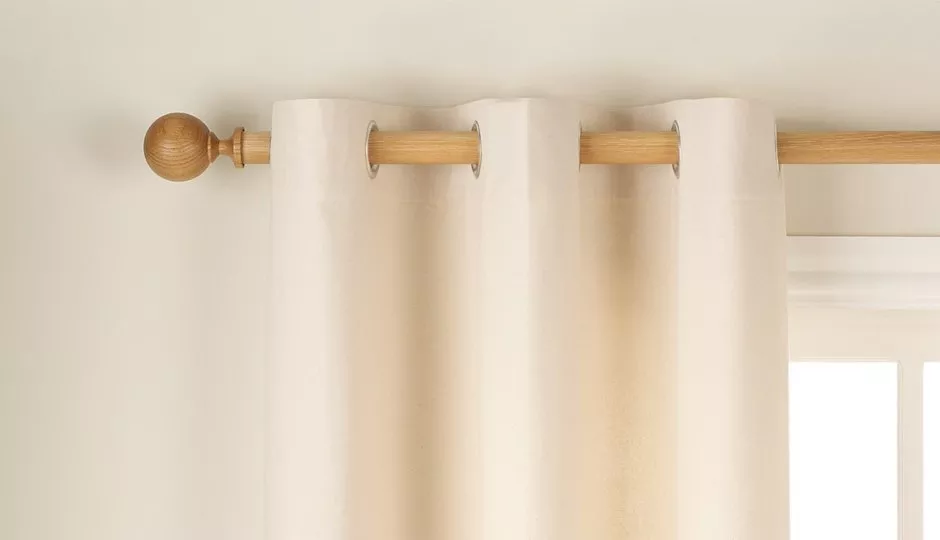 Cream eyelet curtains hanging on a wooden curtain pole with round finial, minimalist window dressing detail
