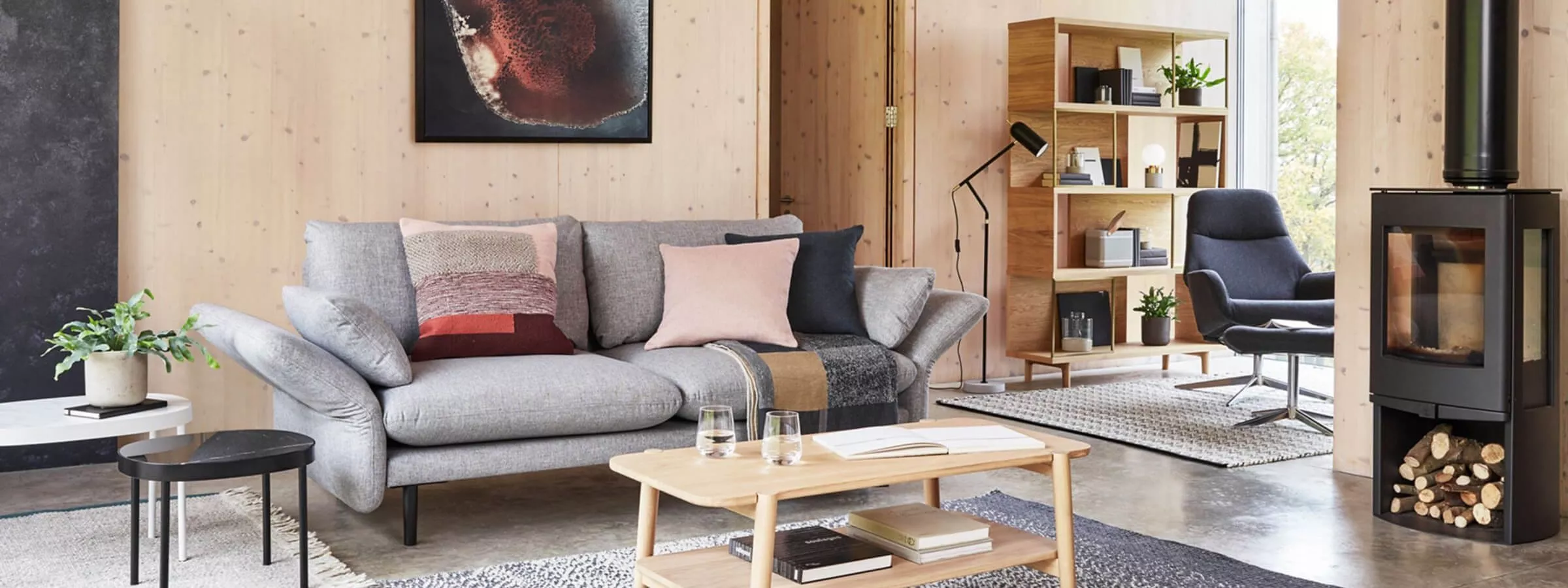 Modern Scandinavian living room with grey sofa, wooden coffee table, bookcase, armchair and wood-burning stove