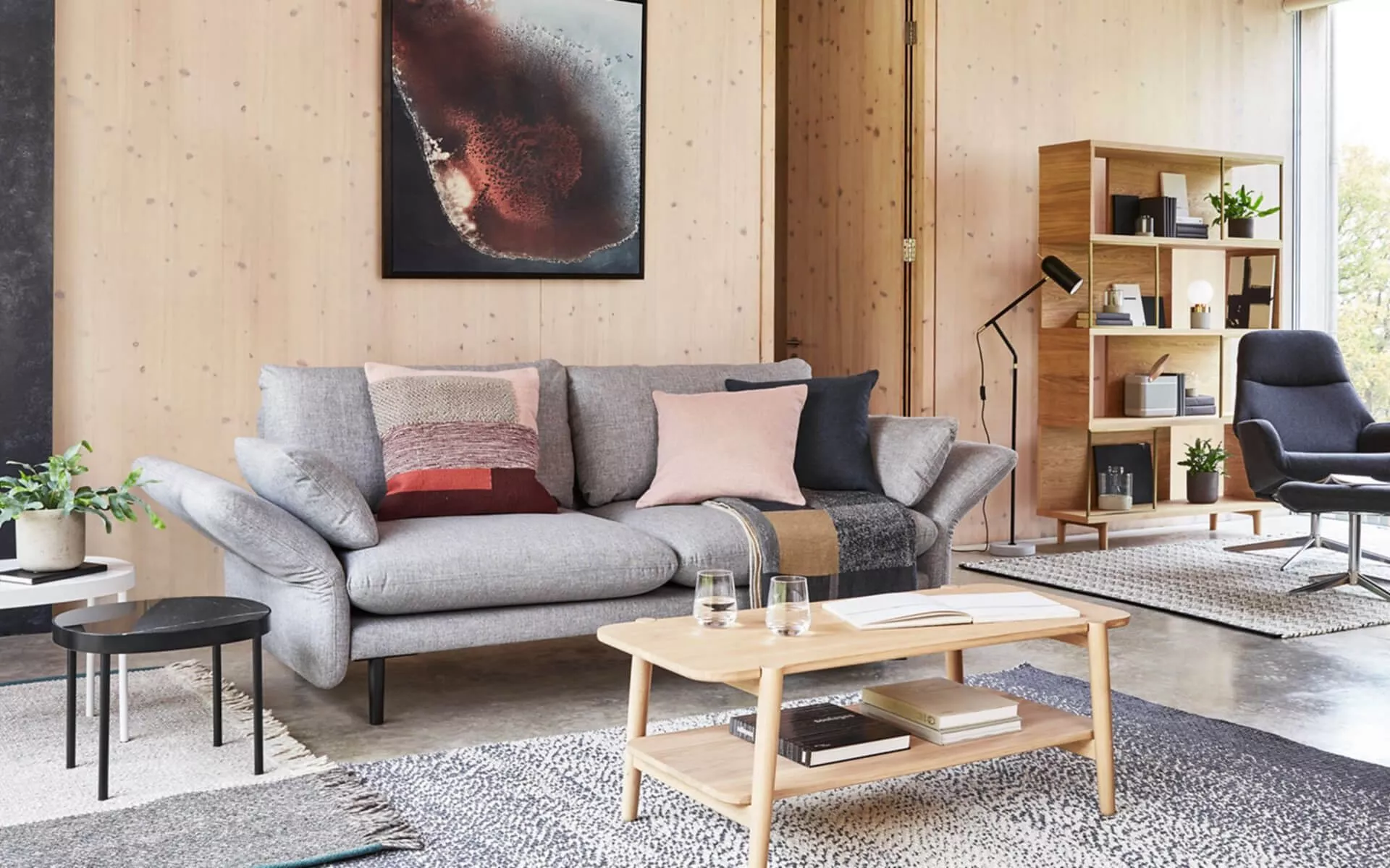 Modern Scandinavian living room with grey fabric sofa, wooden coffee table, shelving unit and abstract wall art