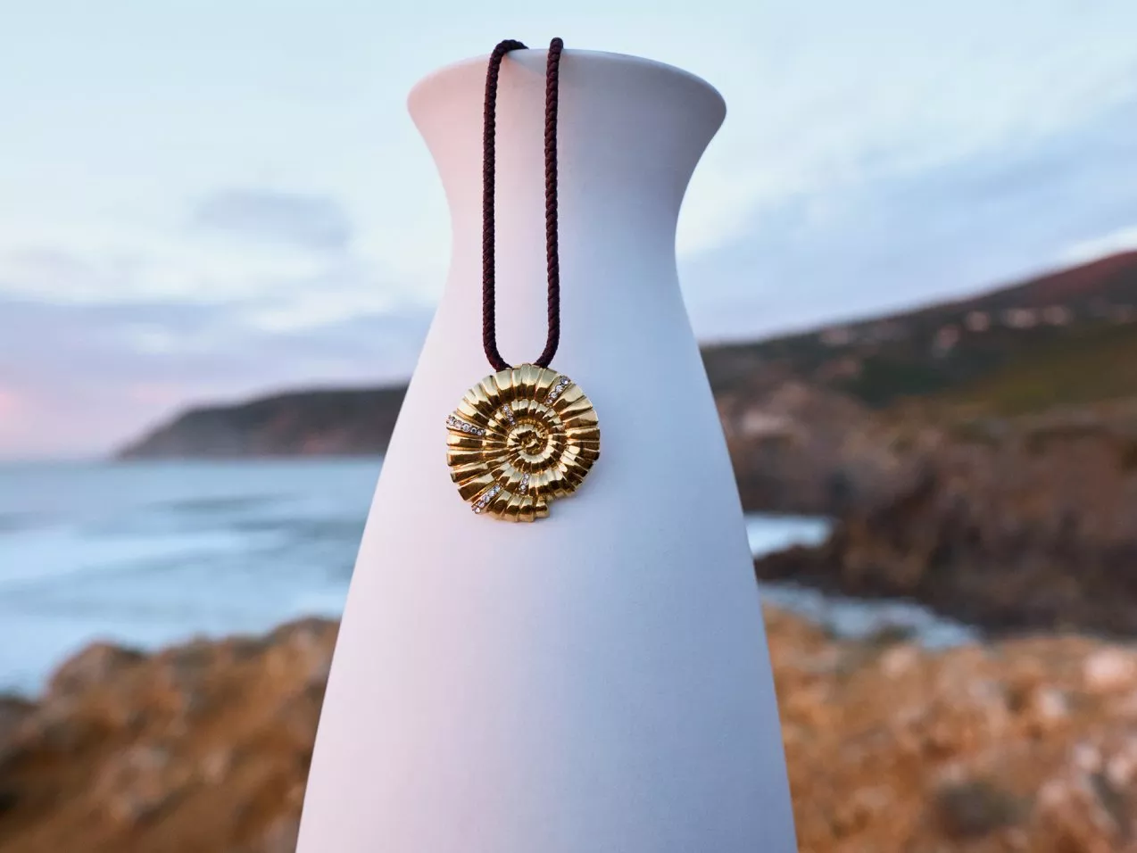 Golden spiral pendant on a vase with a coastal backdrop, showcasing a blend of elegance and natural beauty.