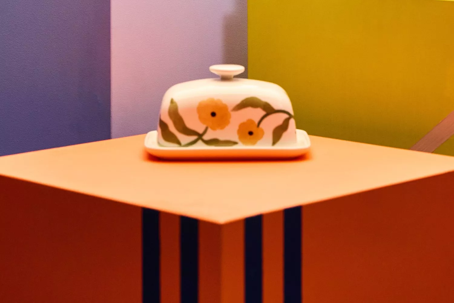 Colourful ceramic butter dish with floral design on an orange and blue-striped table, vibrant background.