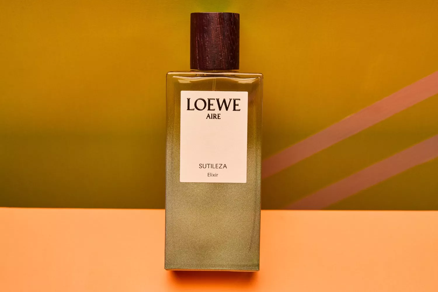 Loewe Aire Sutileza Elixir bottle against a vibrant orange and green background, showcasing elegant design.