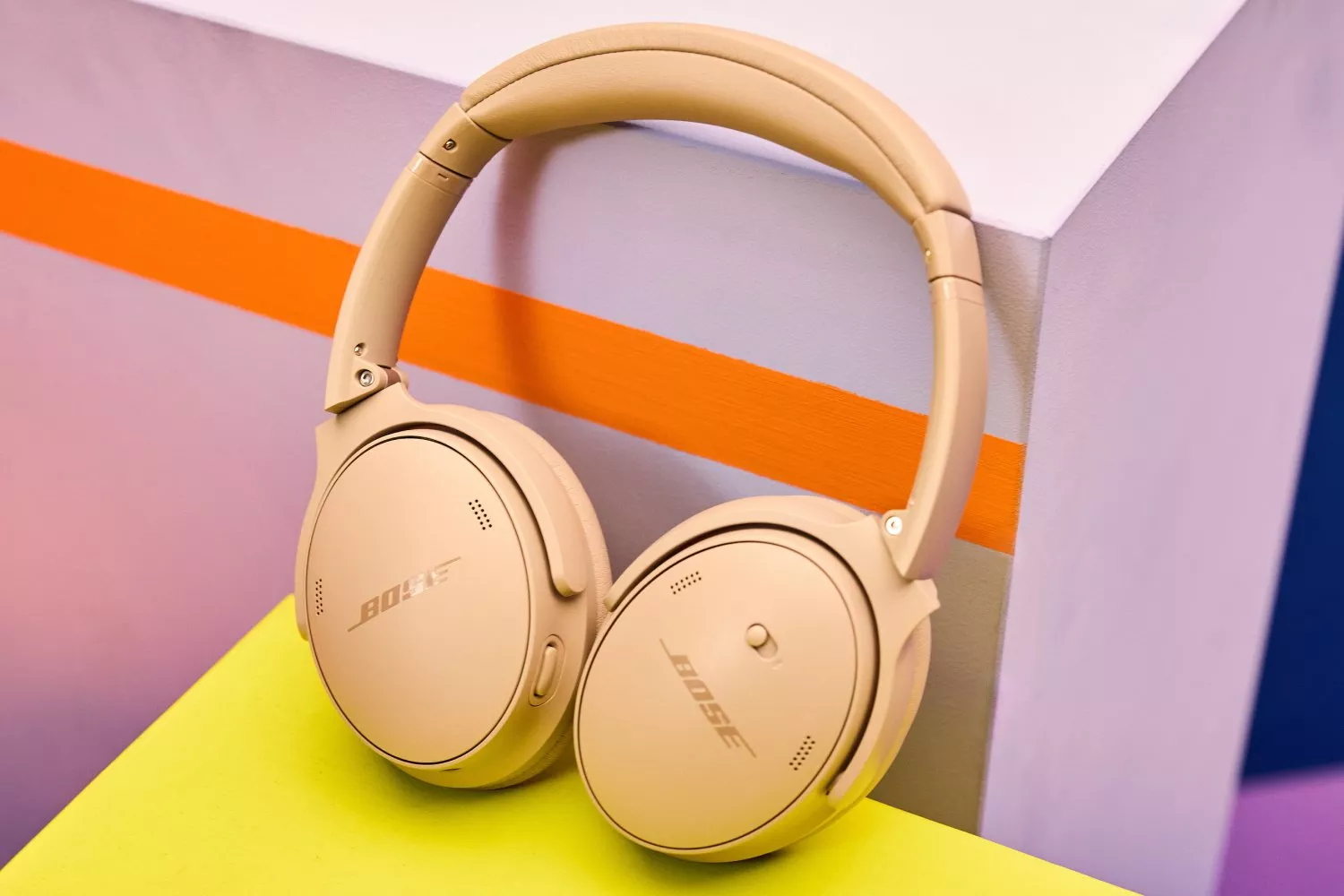 Beige Bose wireless headphones rest on a colourful surface with orange and purple accents in the background.