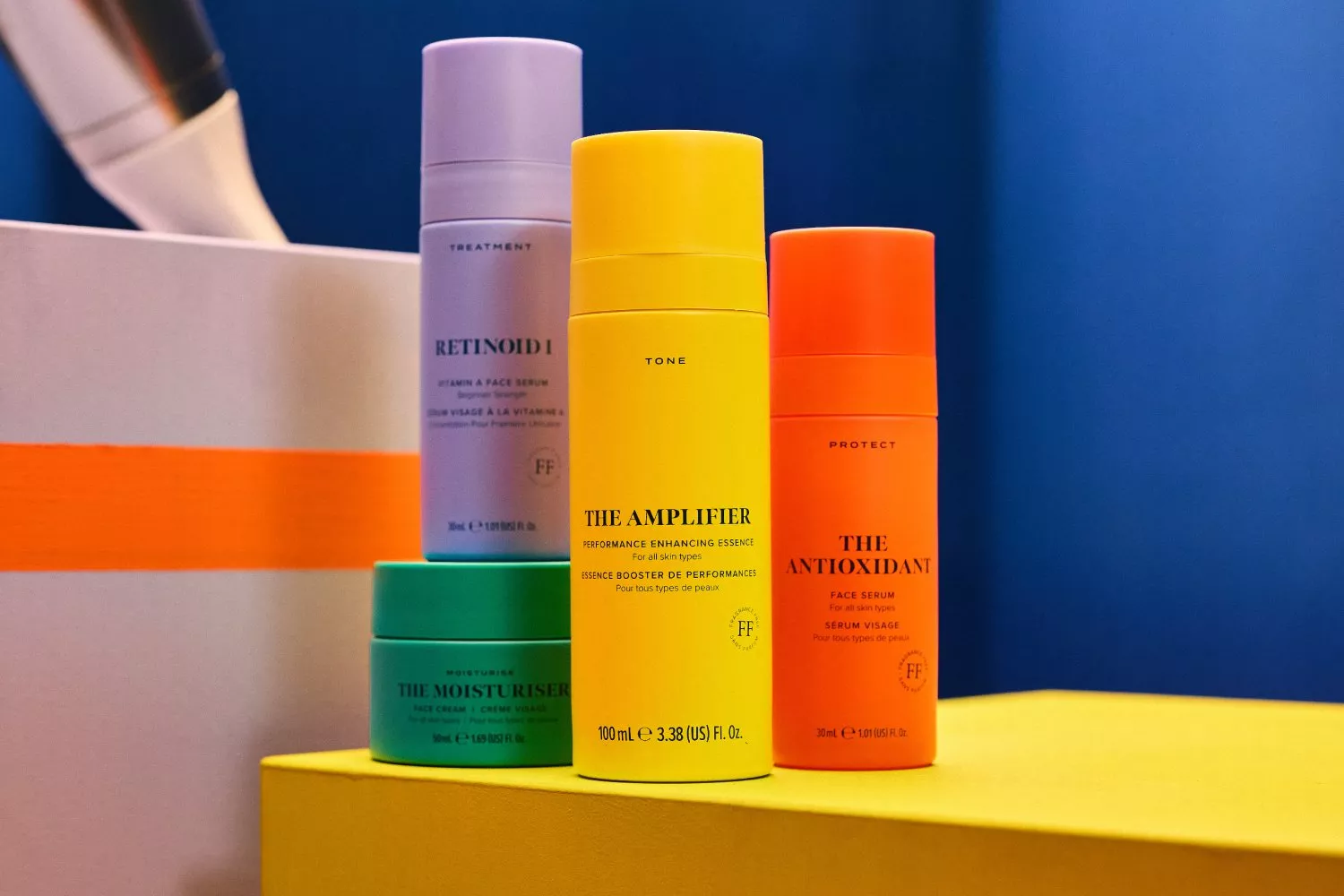 Colourful skincare products displayed on a yellow surface against a blue background, featuring serums and moisturisers.