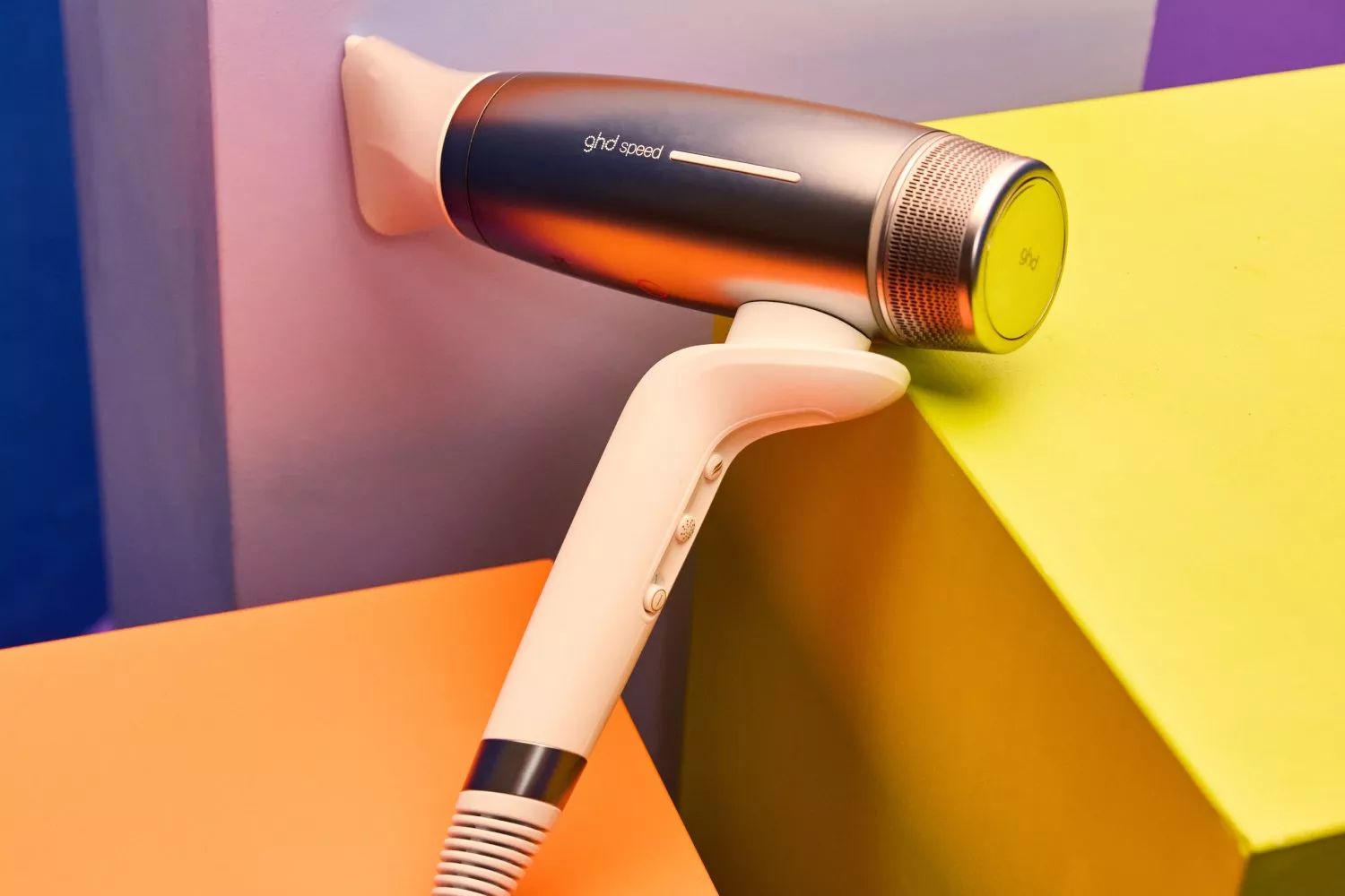 A sleek ghd hairdryer rests stylishly against colourful geometric blocks, highlighting its modern design.