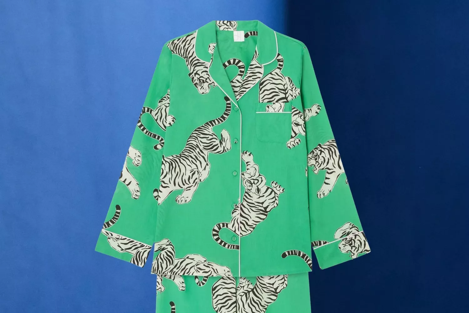 Green pyjama set with playful tiger print on a blue background, featuring a button-up shirt with piping detail.