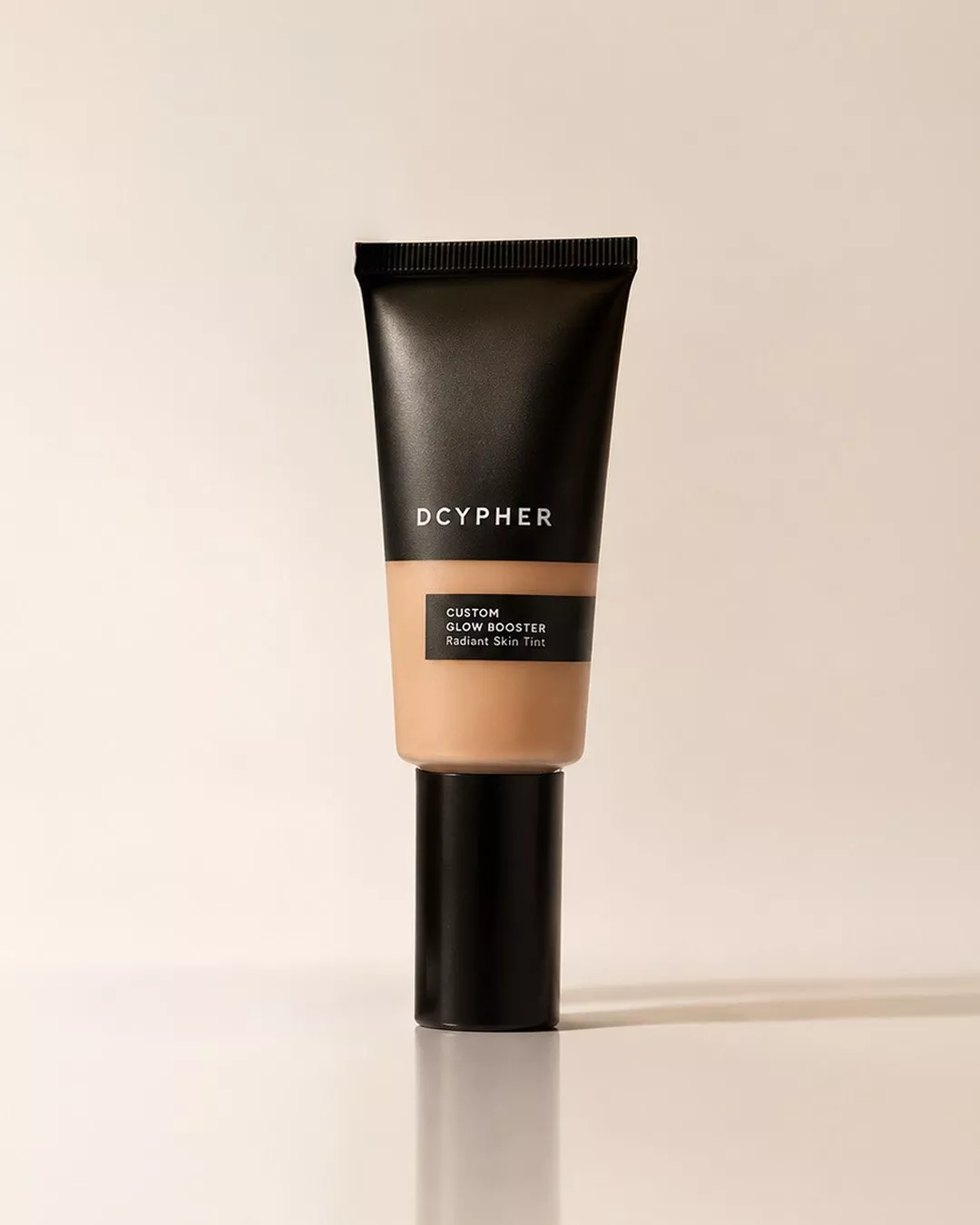 DCYPHER Custom Glow Booster radiant skin tint tube in beige, standing upright on a neutral studio background