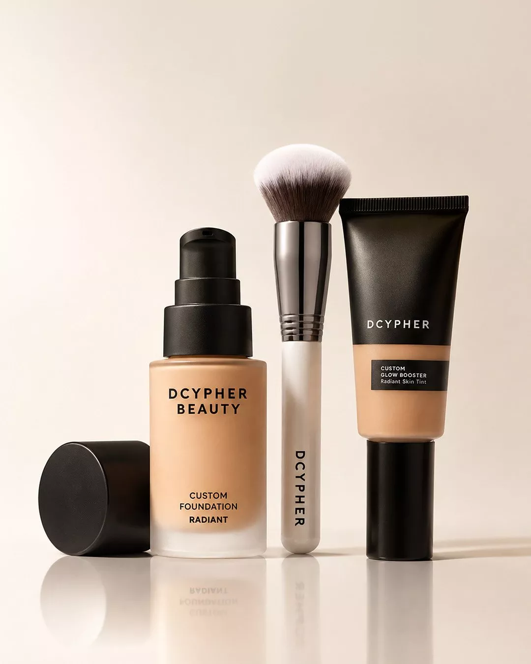 DCYPHER Beauty custom radiant foundation, glow booster skin tint and makeup brush on a beige background.