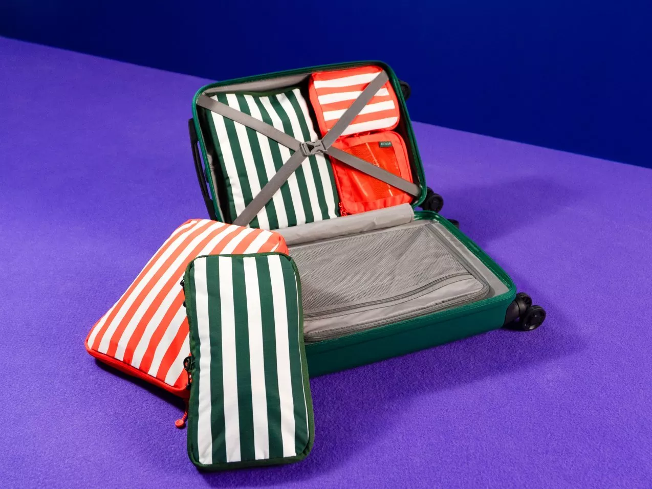 Open green suitcase with striped packing cubes on purple carpet, organised travel luggage storage accessories