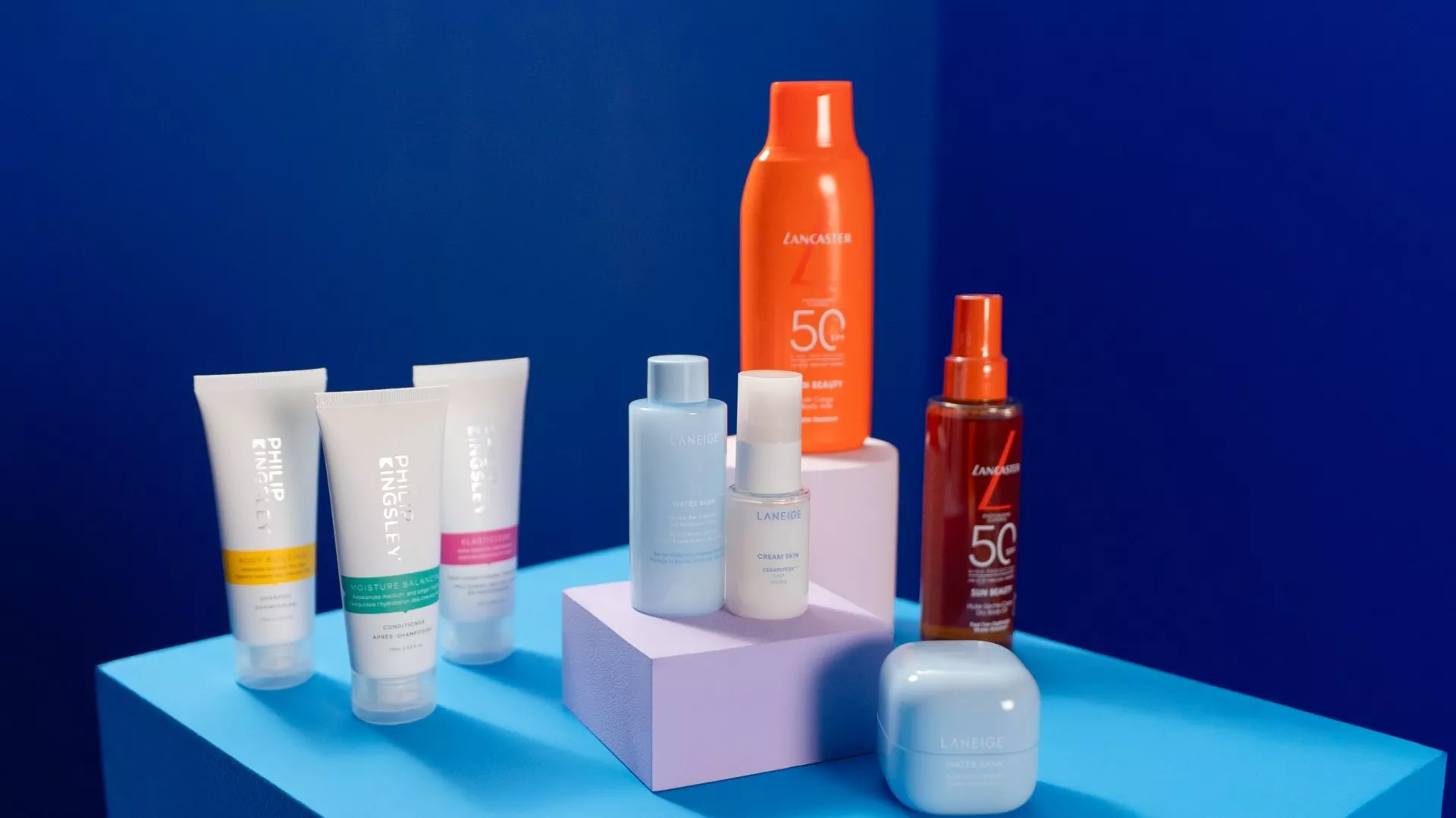 Skincare and sun care products on blue display, featuring SPF 50 spray, moisturiser bottles and travel tubes.