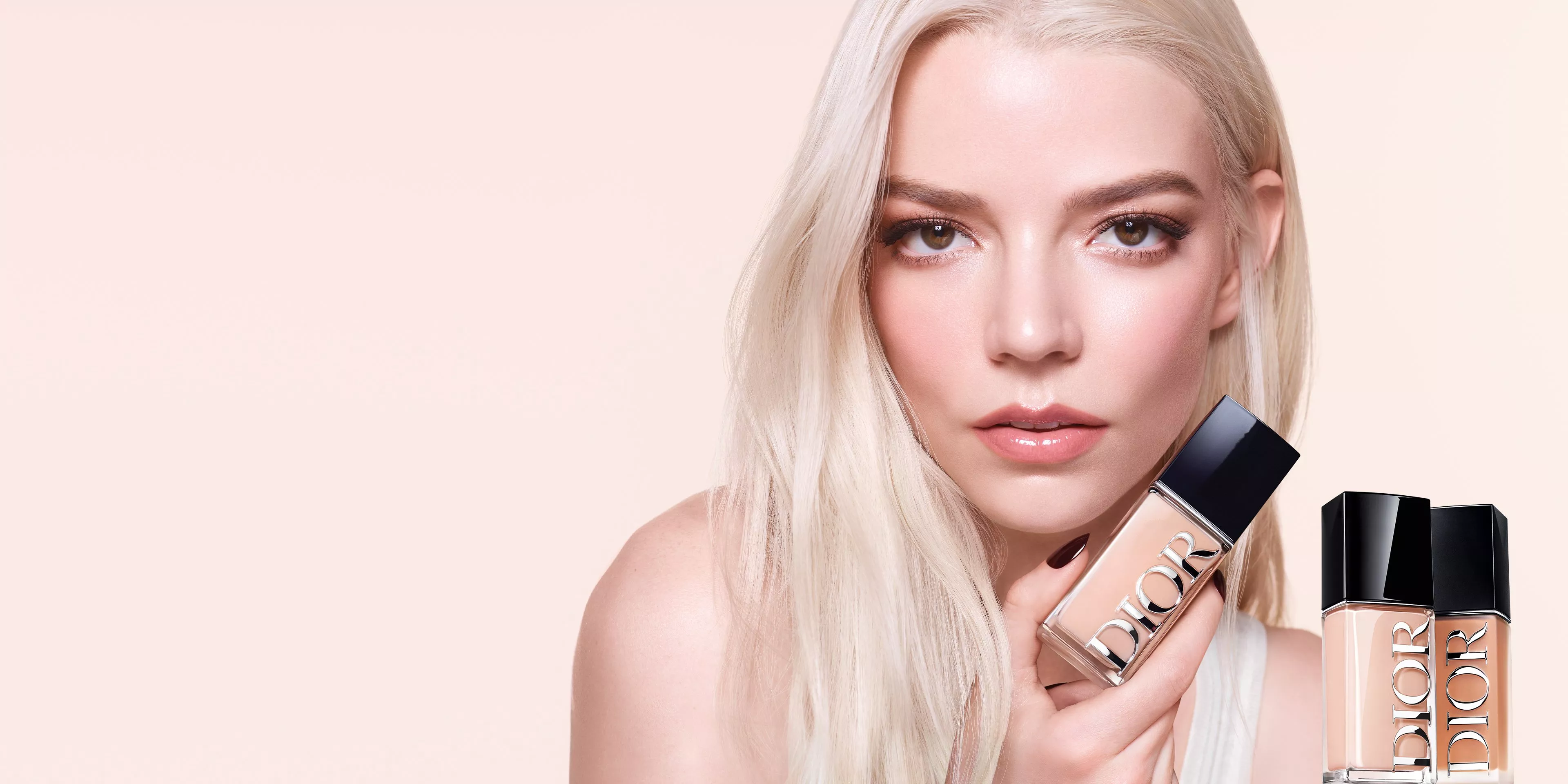 A person with long blonde hair holds a Dior foundation bottle. Another bottle is displayed nearby.