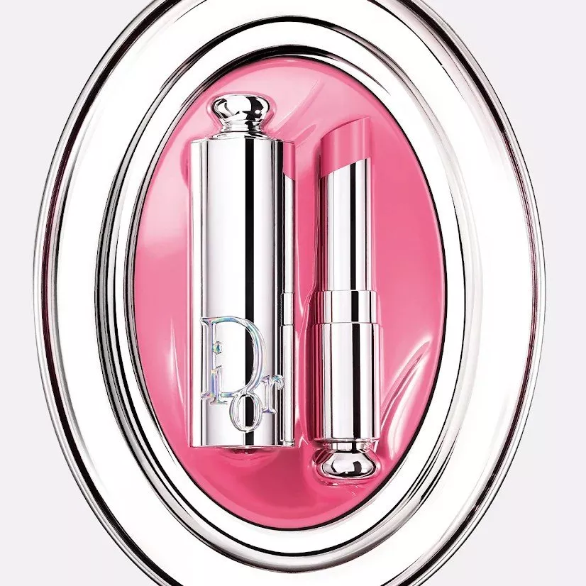 Elegant display of Dior lip glosses in pink and burgundy shades on a decorative white background.