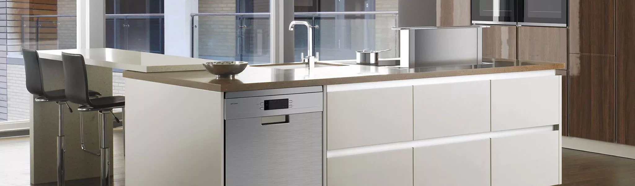 Modern kitchen island with white cabinets, stone worktop, breakfast bar stools and built-in dishwasher by window