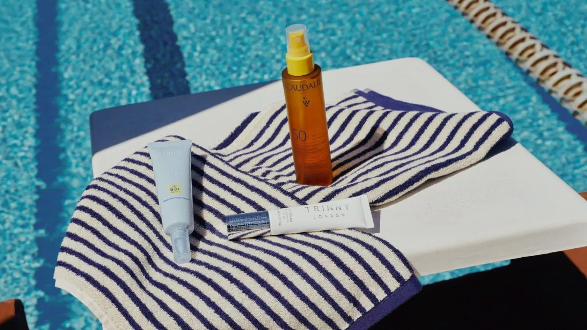 Sunscreen and skincare products on a striped towel by a pool, summer sun protection essentials close-up