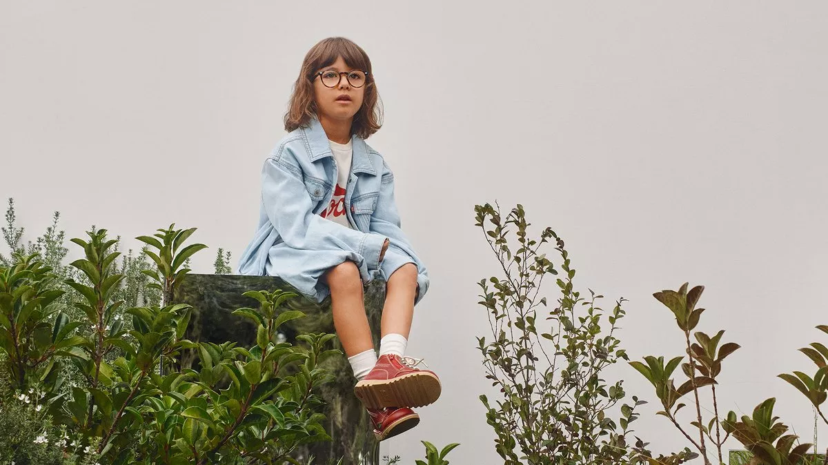 Child wearing denim jacket and glasses sitting on stone block in garden, casual kids fashion outdoors
